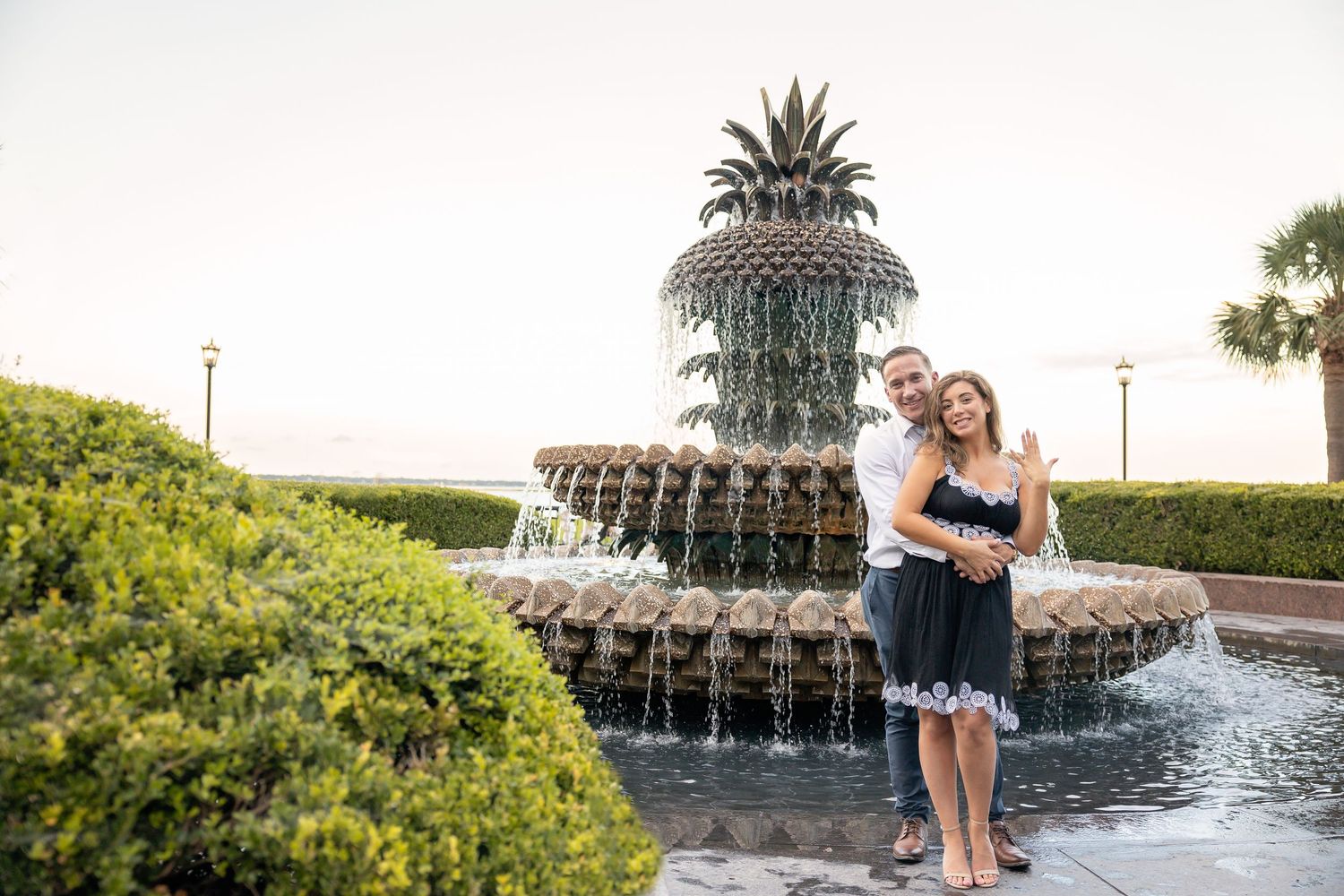 Waterfront engagement session featuring pineapple fountain and palm trees at golden hour.