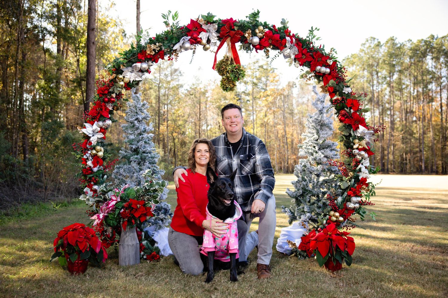 Beautiful outdoor Christmas photo setup with red floral arch and snowy trees in a wooded setting.
