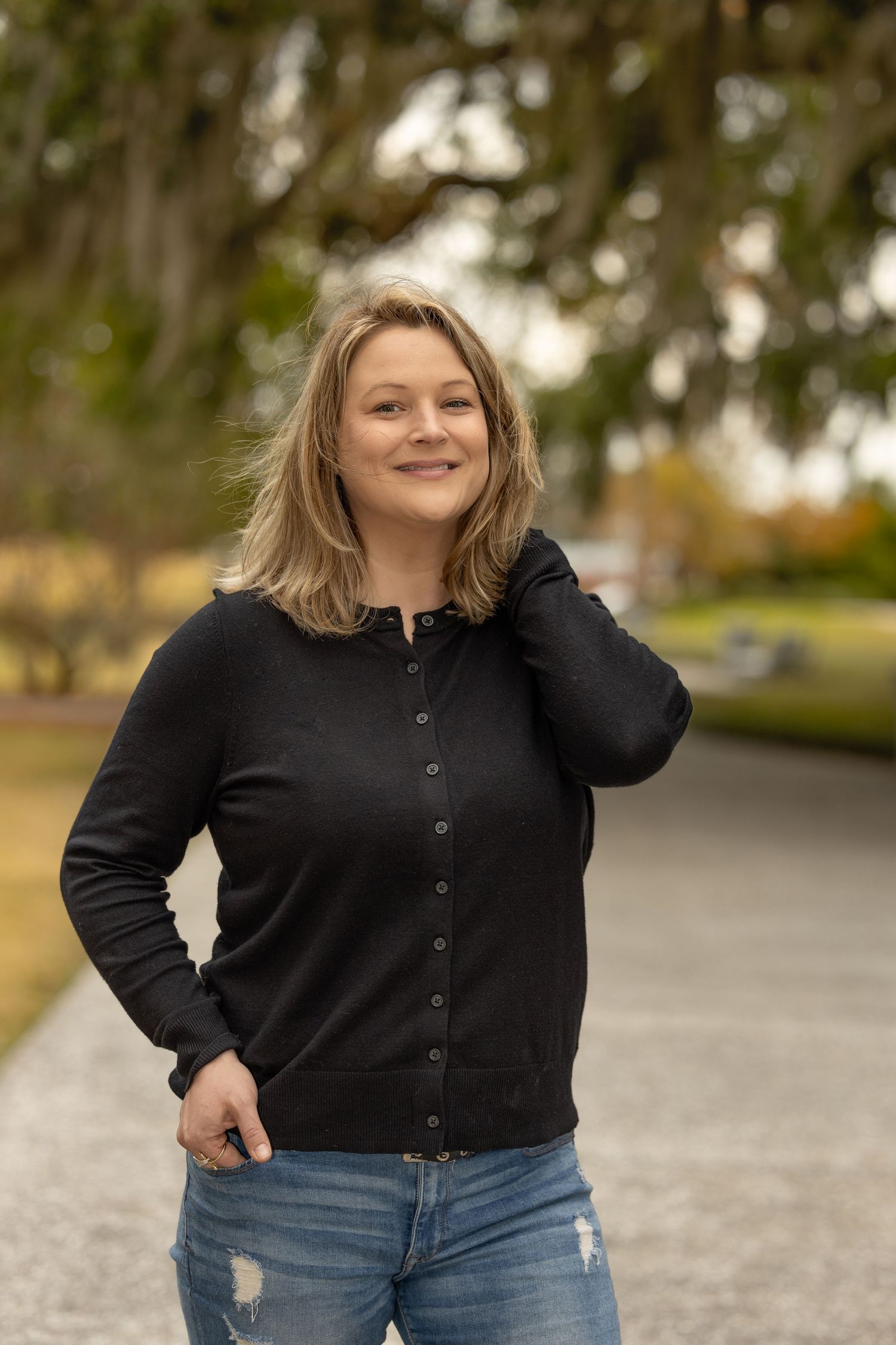 Woman in black cardigan posing outdoors in autumn setting.