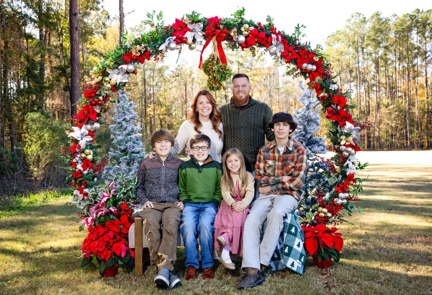 Holiday family photos under decorative red and white floral arch in outdoor setting.