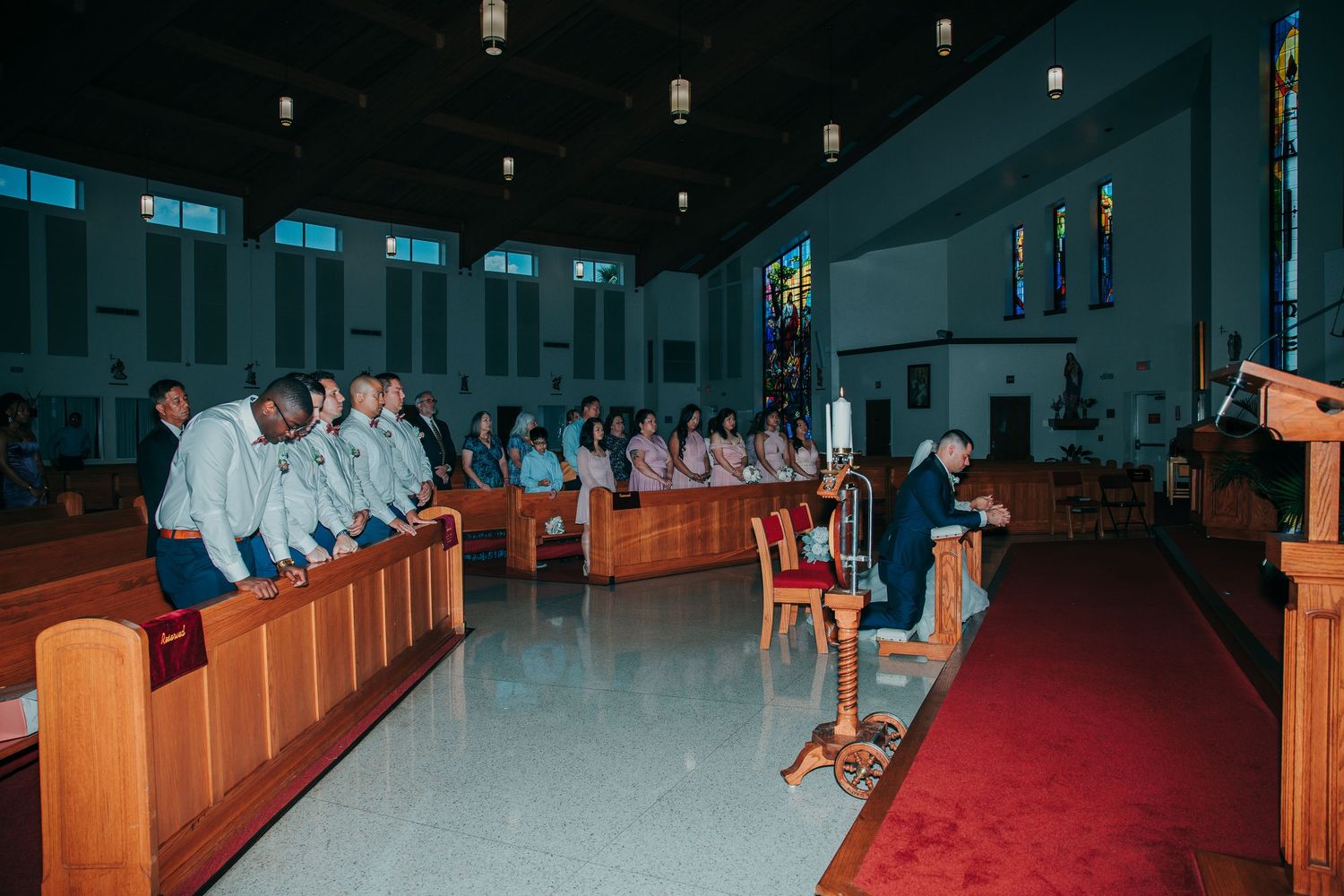 Wide angle view of a church wedding ceremony with guests seated in wooden pews.