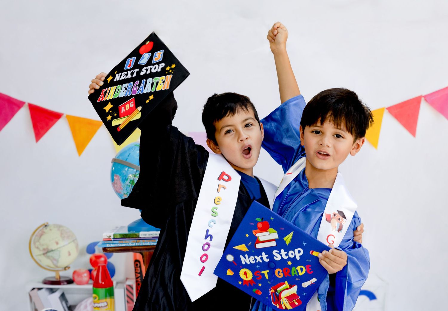 Kids celebrate graduation with decorated caps and festive backdrop.
