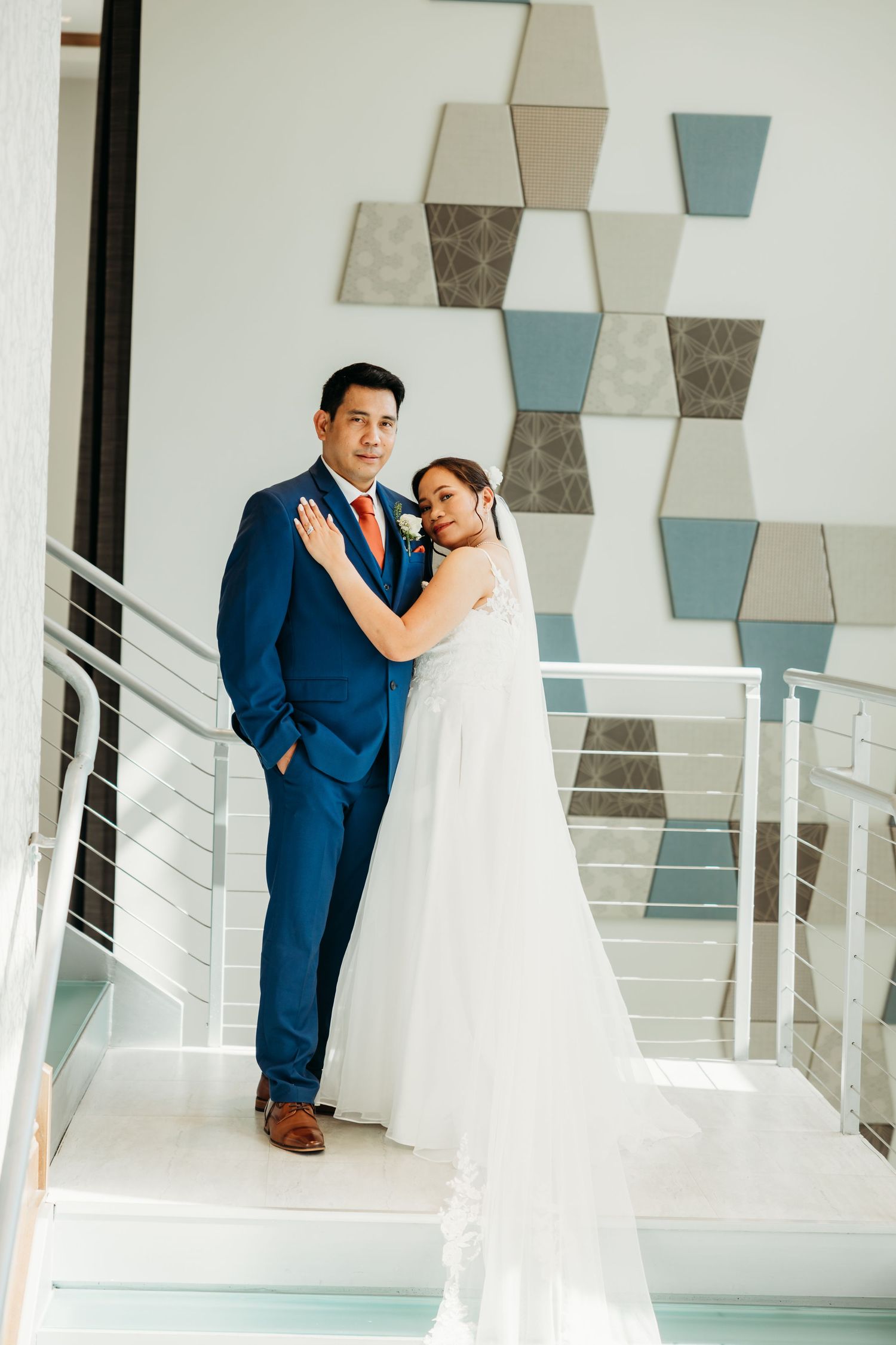 Newlyweds embracing in an elegant white venue with geometric wall art.