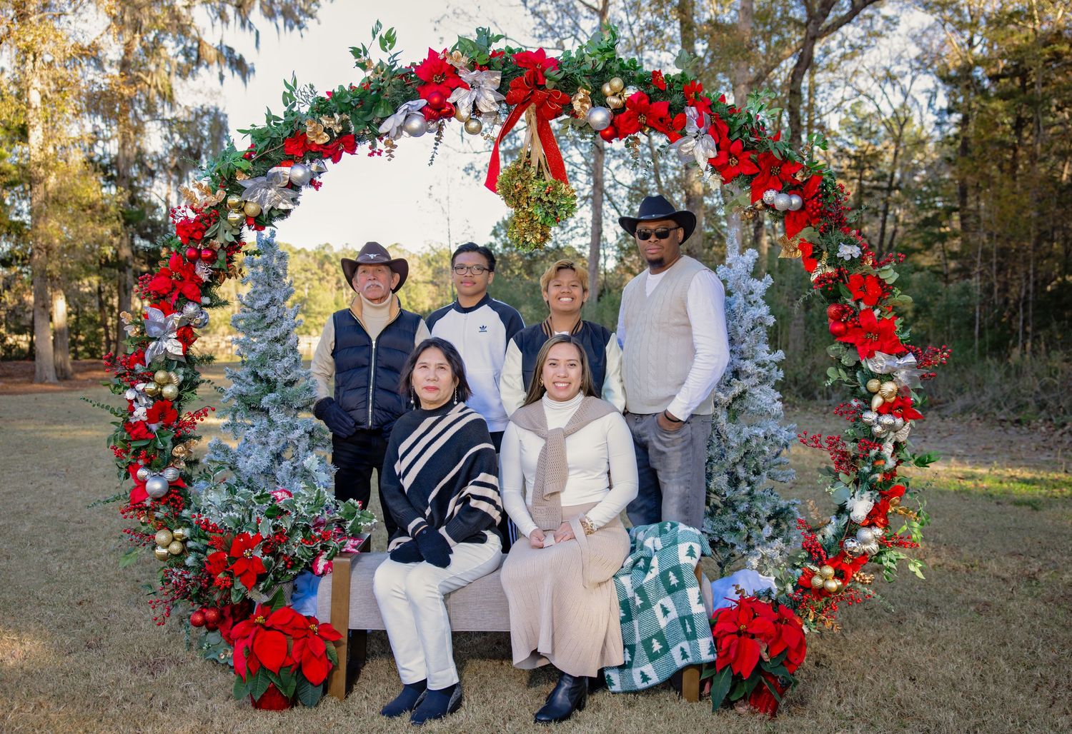 Family portrait session under large Christmas-themed wedding arch with red flowers and greenery.
