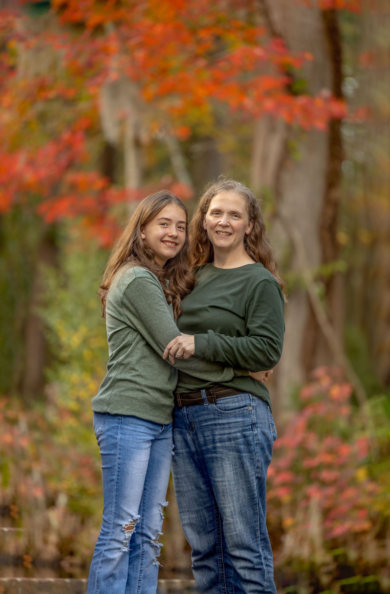 Two people in casual outfits share a laugh together against a backdrop of vibrant fall foliage.
