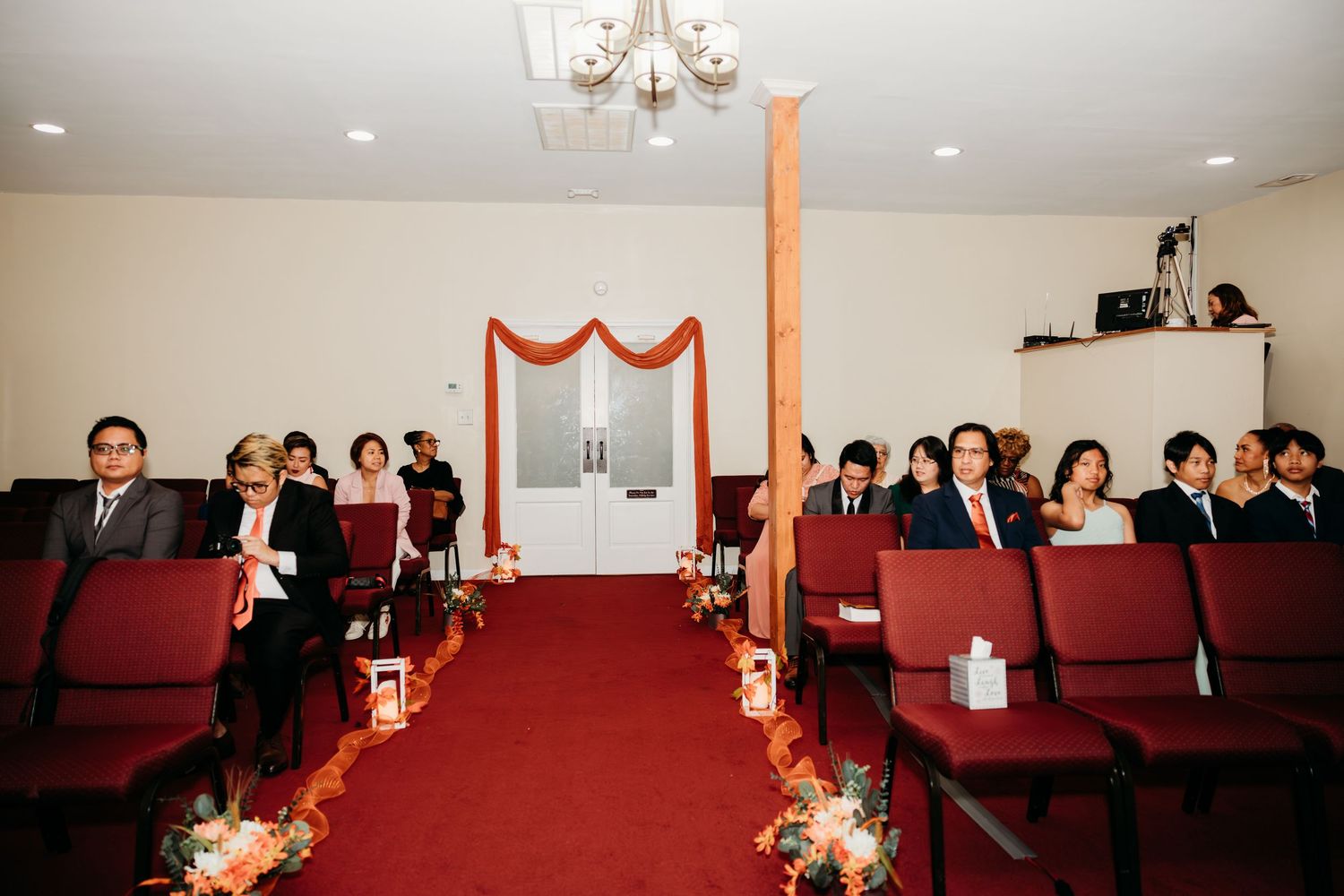 Indoor wedding ceremony venue with red carpet aisle and orange fabric decorations.