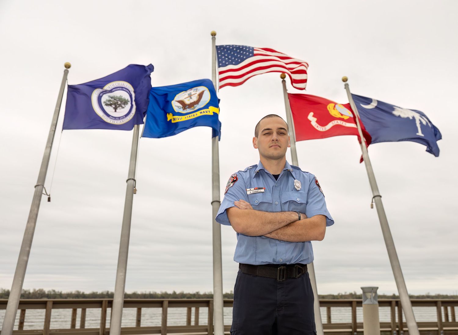 Row of American and military flags flying along waterfront pier.