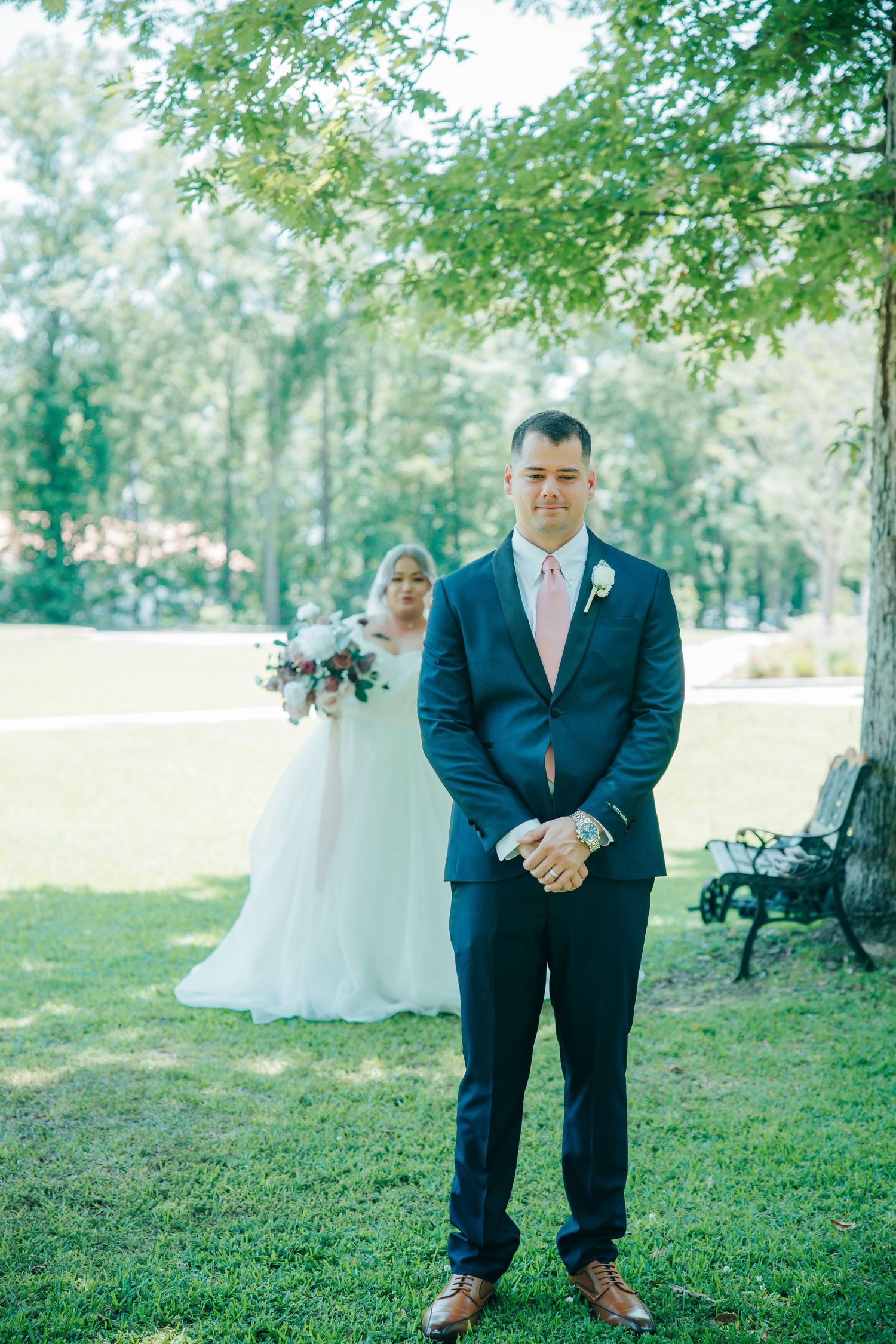 Outdoor wedding venue setup with navy-suited attendants on a lush green lawn.