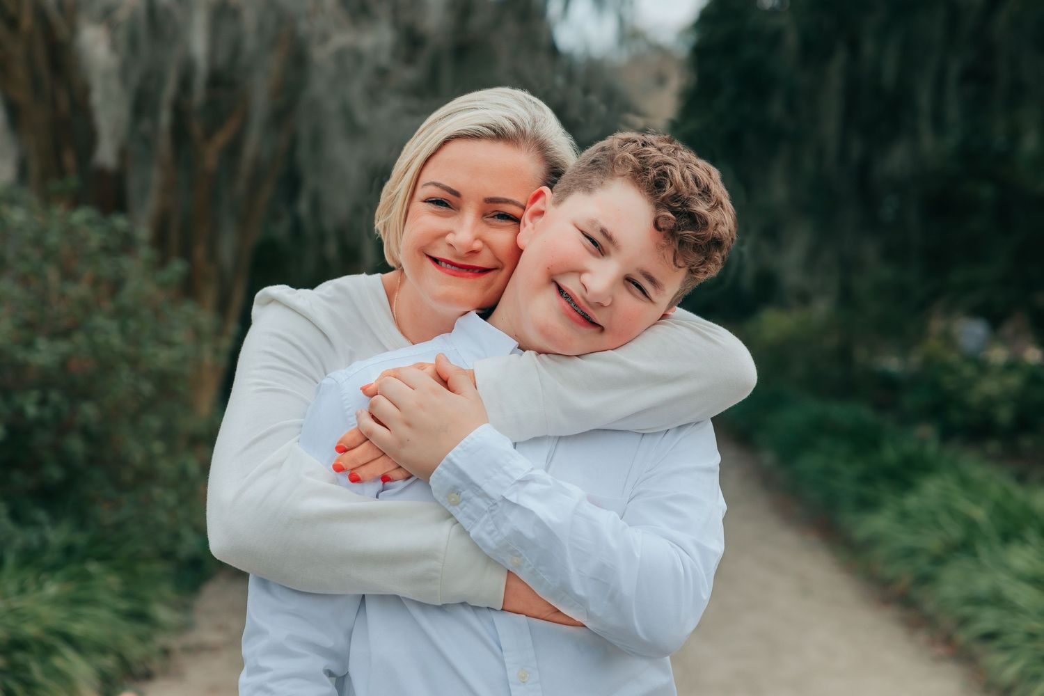 Playful embrace captured on a nature path surrounded by Spanish moss and trees.