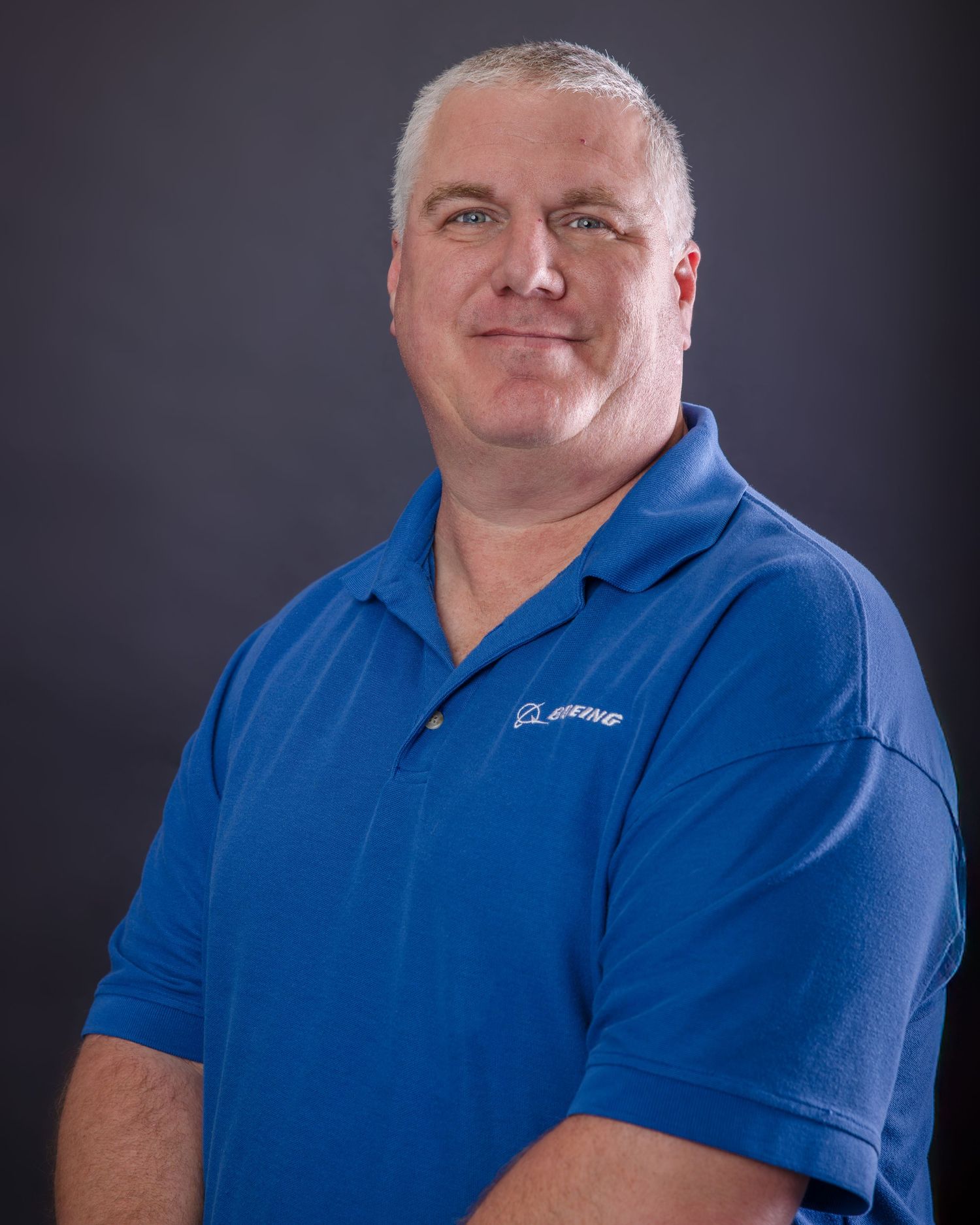 Professional headshot of someone in a blue Boeing polo shirt against dark background.