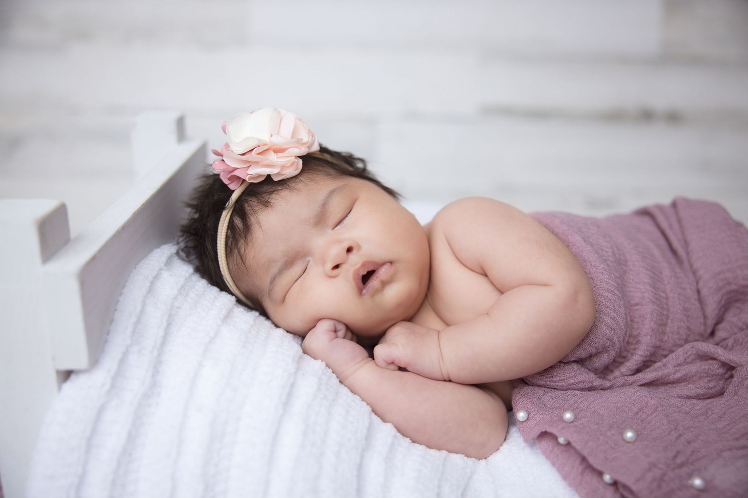 Sleeping newborn in soft purple wrap on white background in minimalist style.