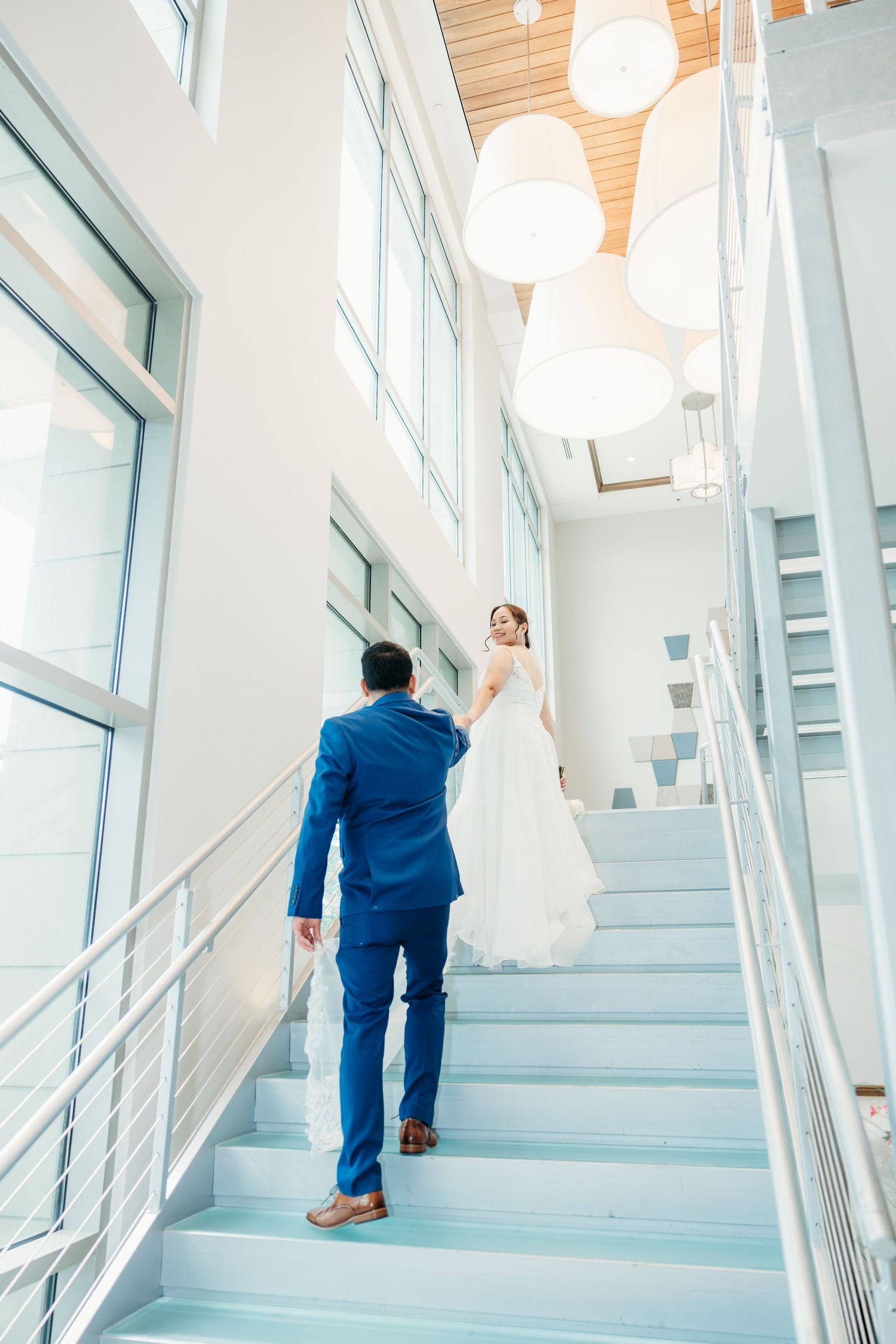 Couple ascends modern blue-tinted staircase during wedding photoshoot.