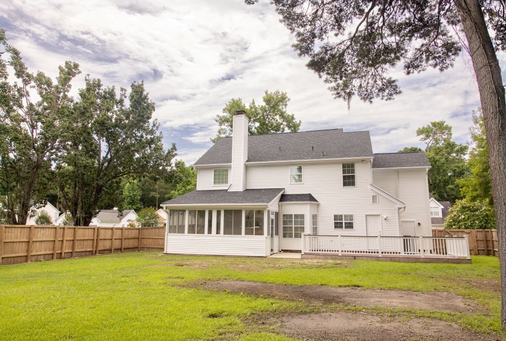 Back exterior view of white two-story home with fenced yard and sunroom.