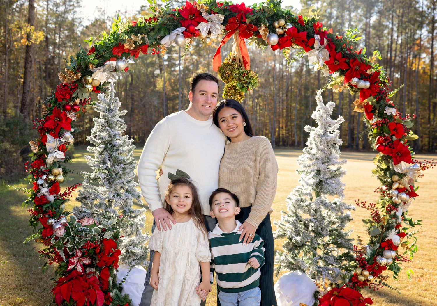 Holiday wedding photos under festive red and white floral arch with pine trees in background.