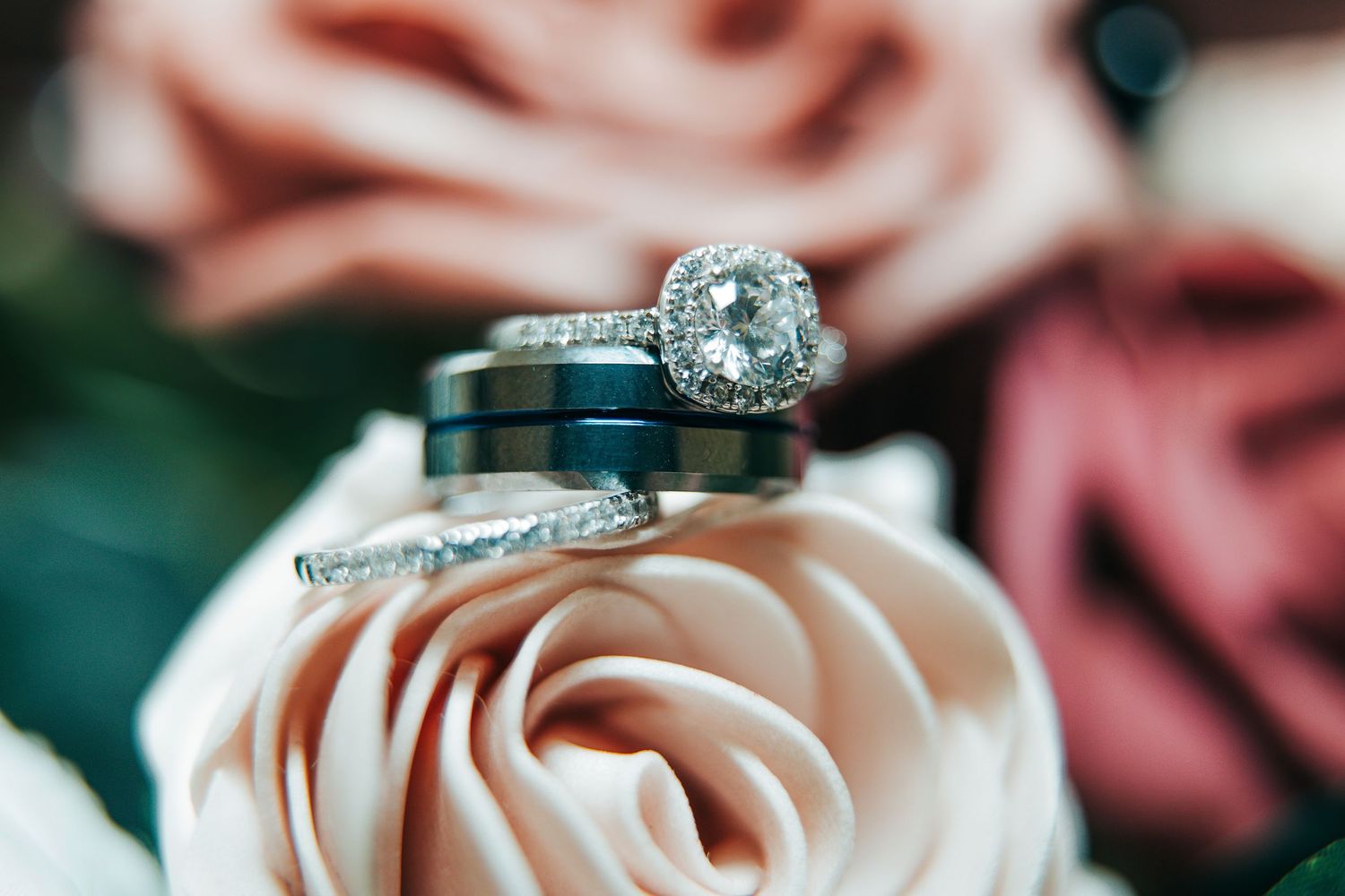 Wedding rings resting on pink and coral roses with a diamond engagement ring and navy blue band.