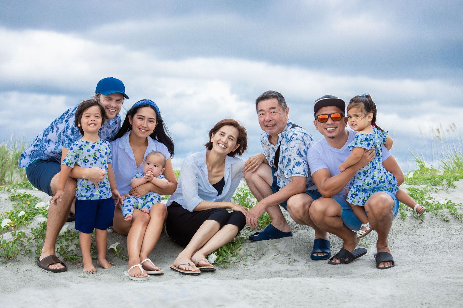 Family wearing coordinated blue outfits poses playfully on a sandy beach.