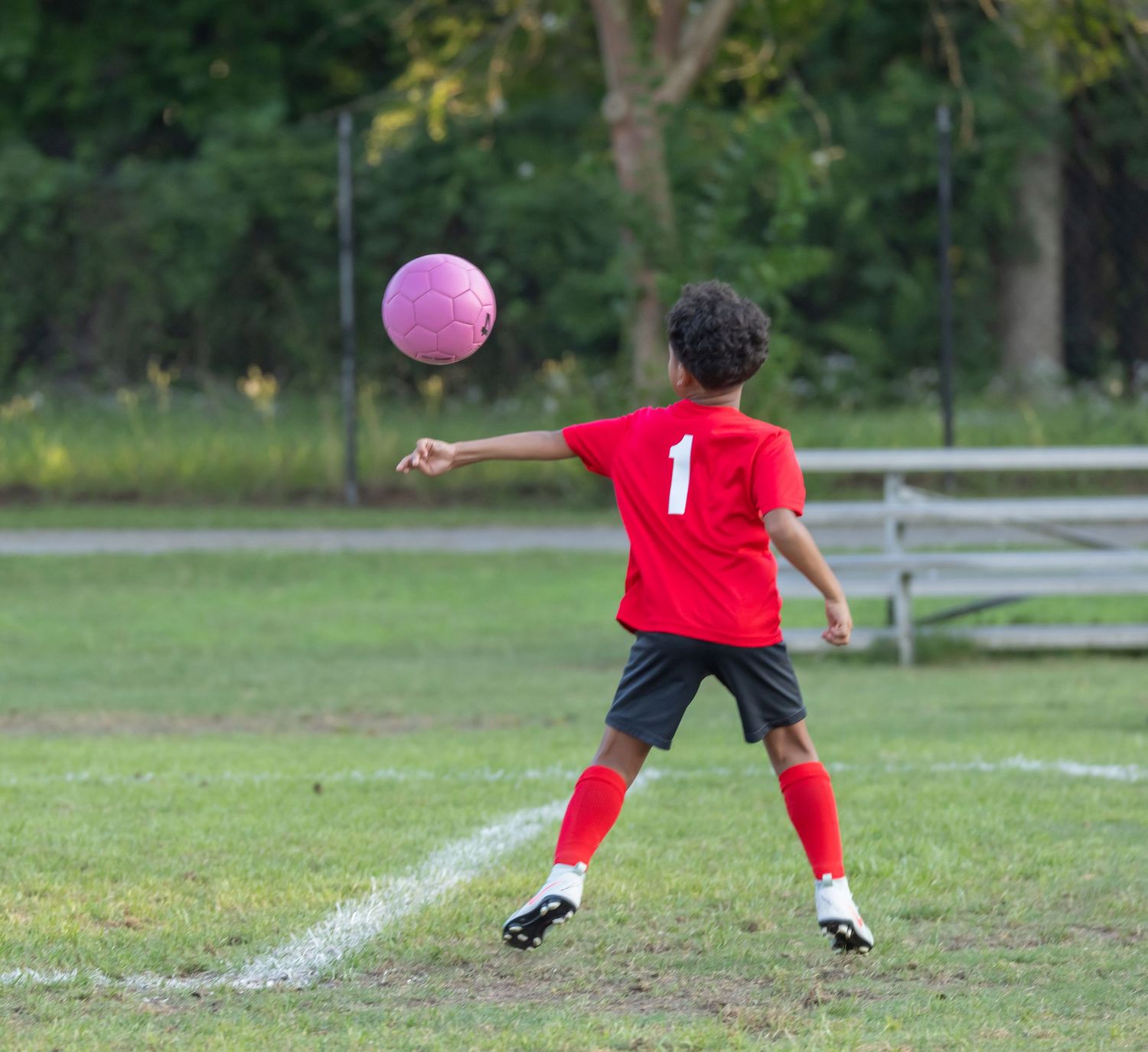 Soccer player in red jersey kicking pink ball on grass field.
