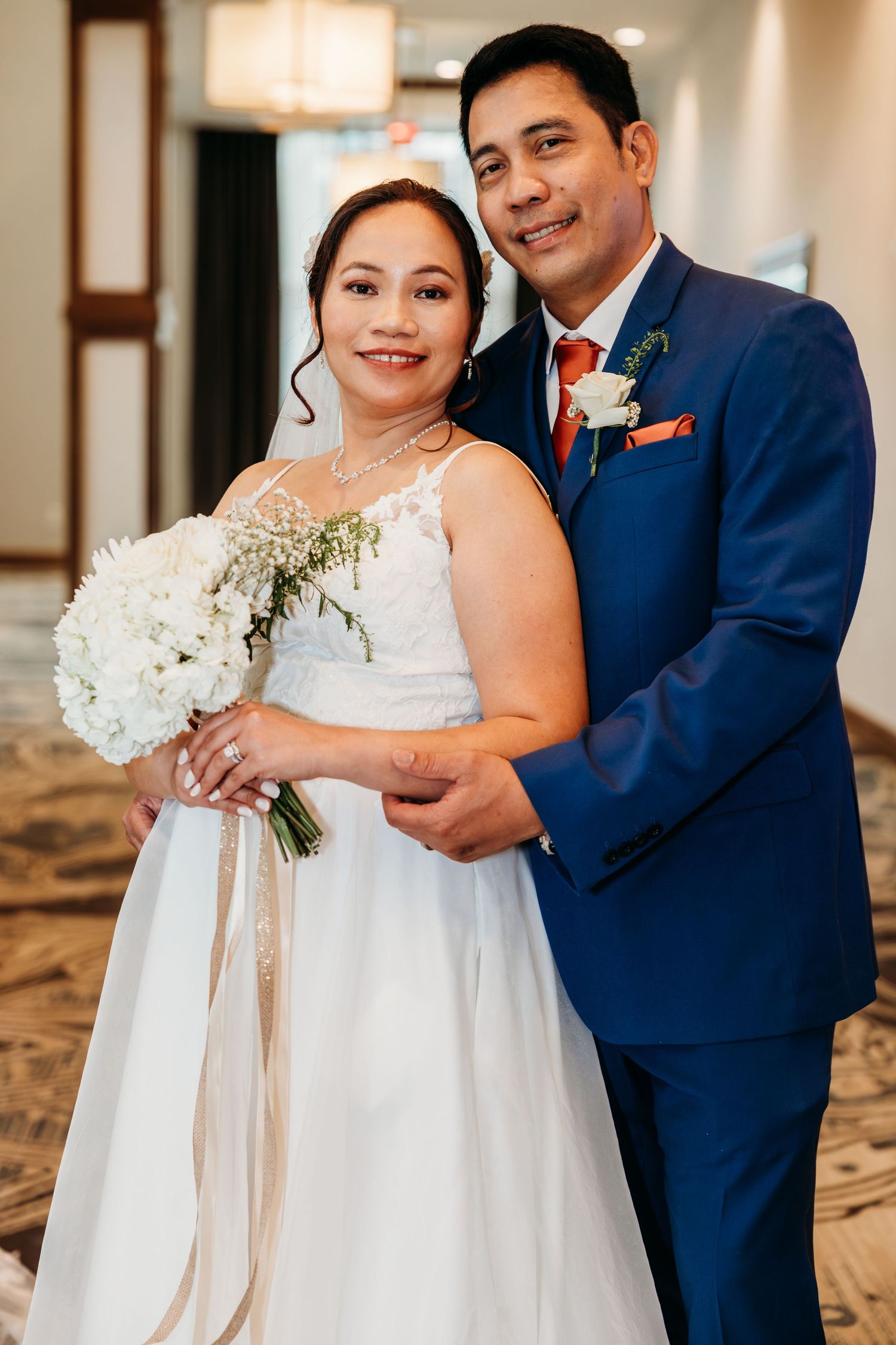 Wedding couple in navy and white attire pose together in an elegant indoor setting.