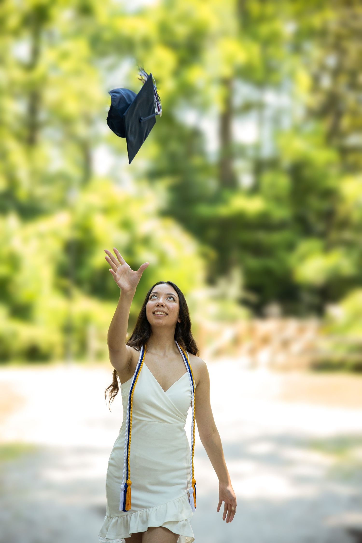 A graduate tosses their cap in celebration outdoors on a sunny day.