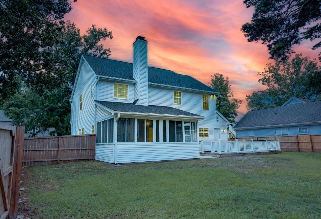 White residential home with covered porch against dramatic orange sunset sky.