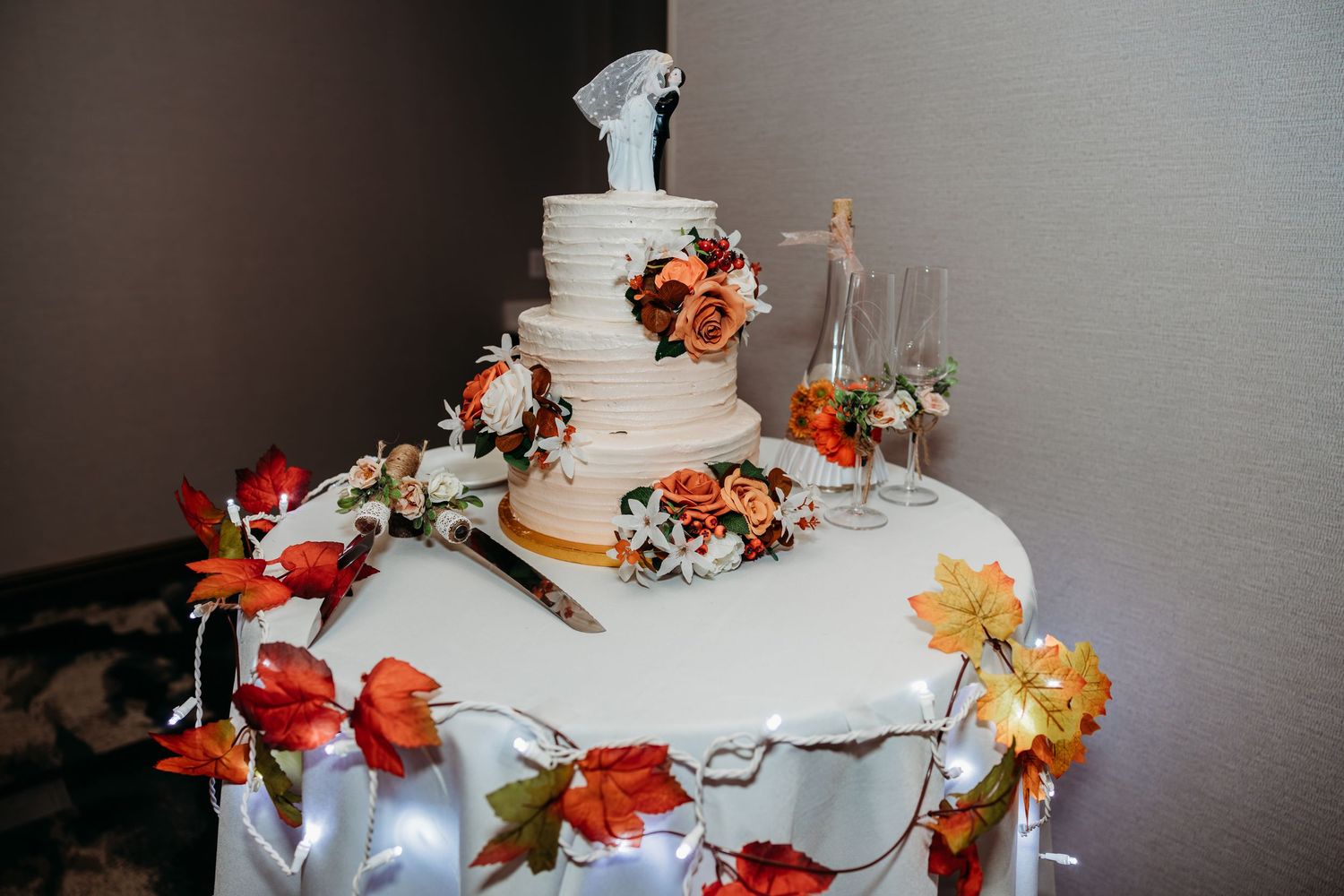 Wedding cake display with autumn-colored floral decorations on a gray table.