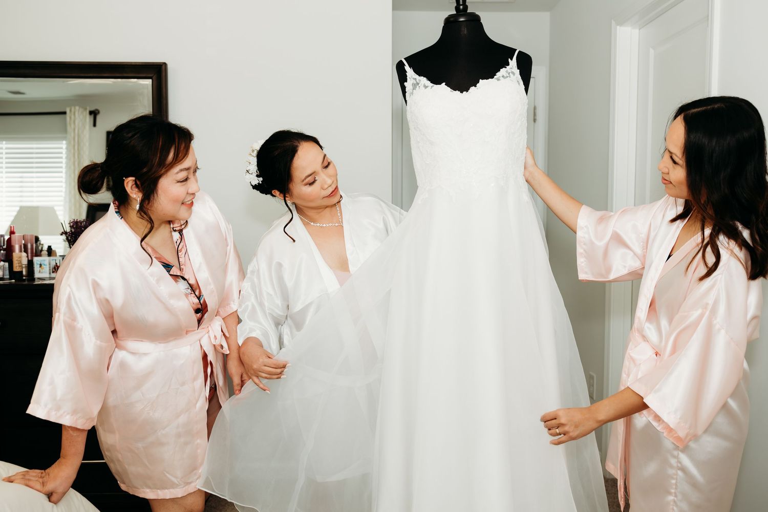 Wedding preparation moments with flowing white dress and pink robes in a sunlit room.