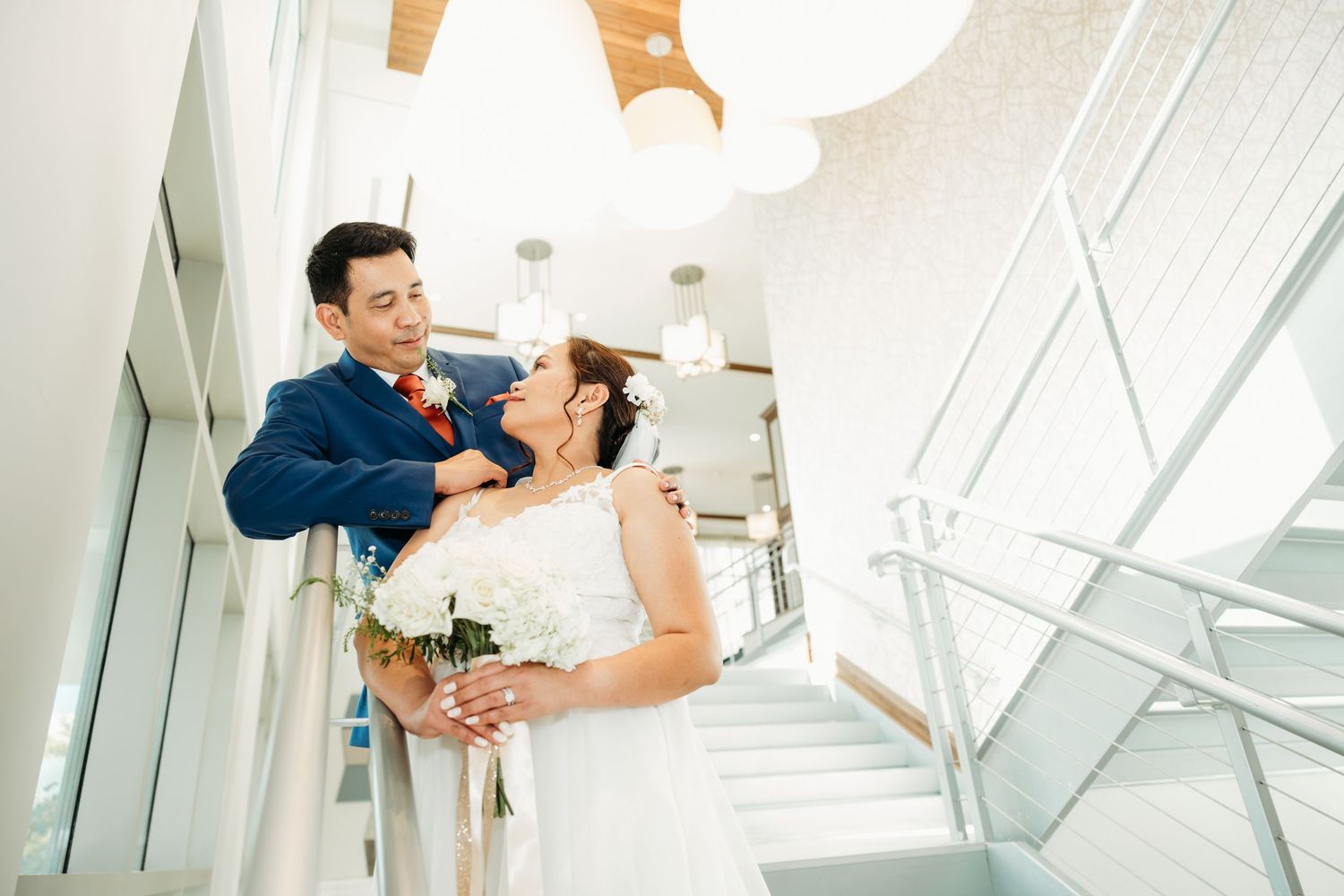 Couple poses playfully on modern architectural staircase during wedding photos.