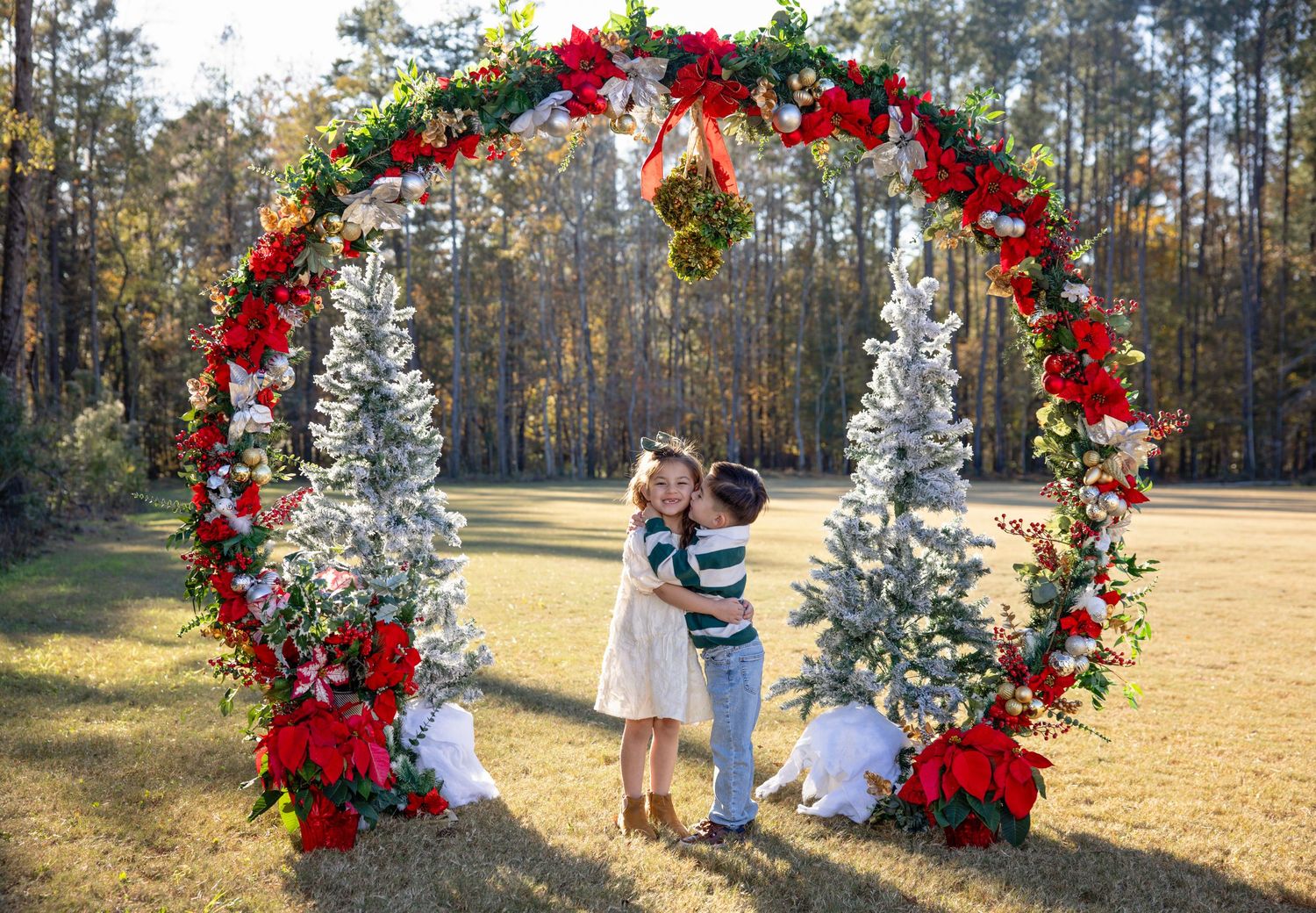 Large Christmas-themed wedding arch with red roses and white decor in outdoor forest setting.