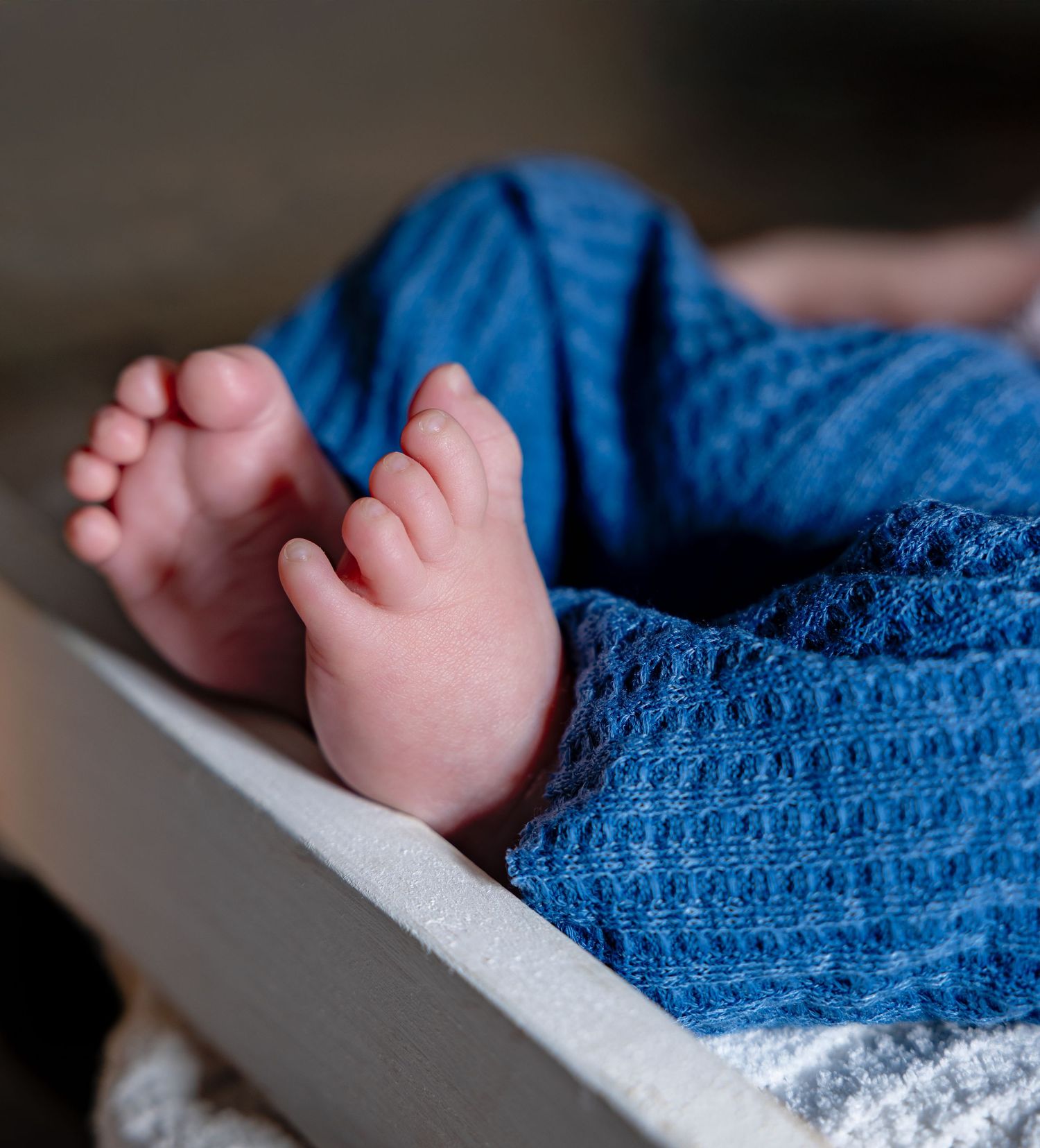 Close-up of tiny feet under a blue knit blanket in newborn photography style.