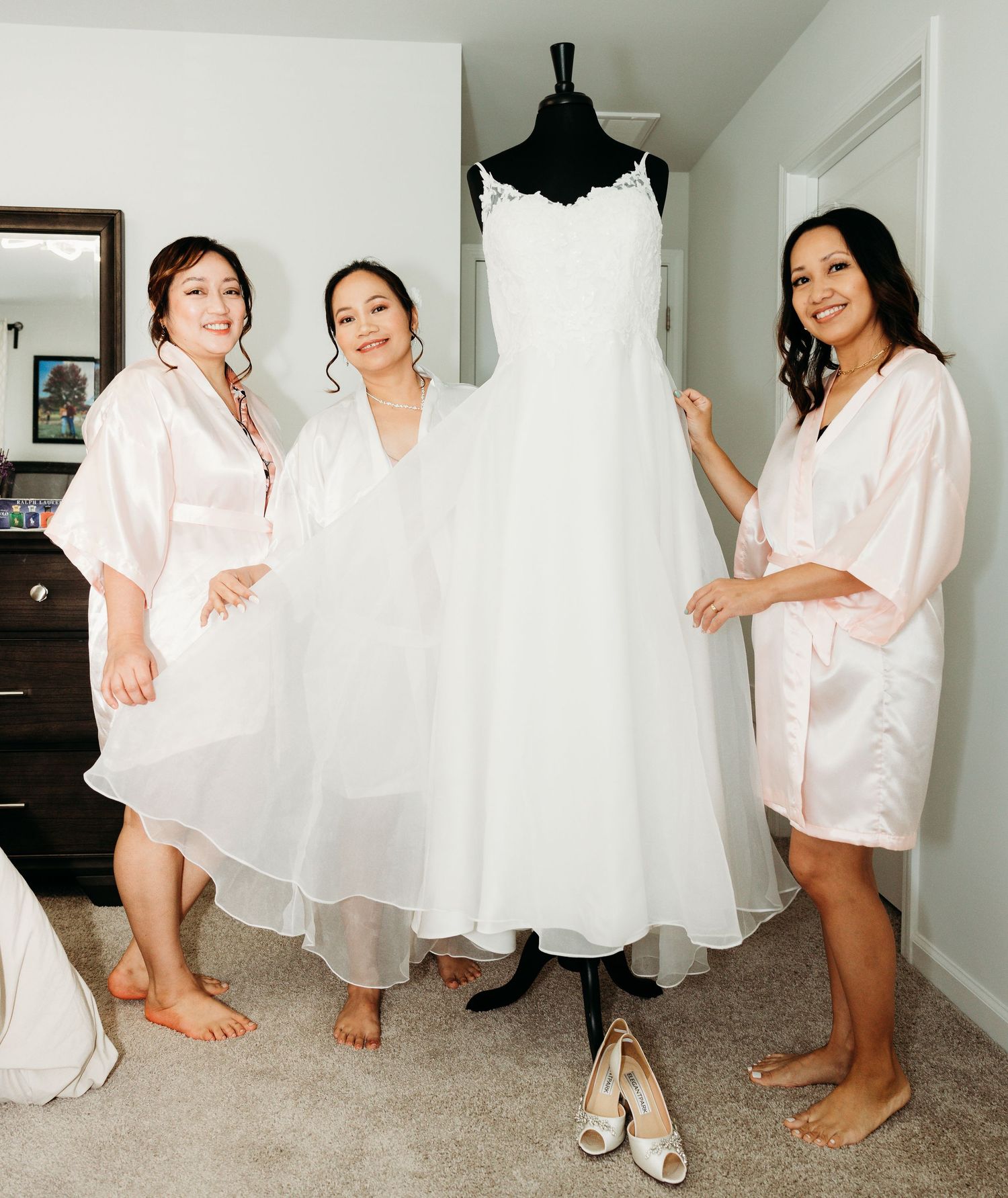 Getting ready scene with white wedding dress and pink robes on display in a bright room.