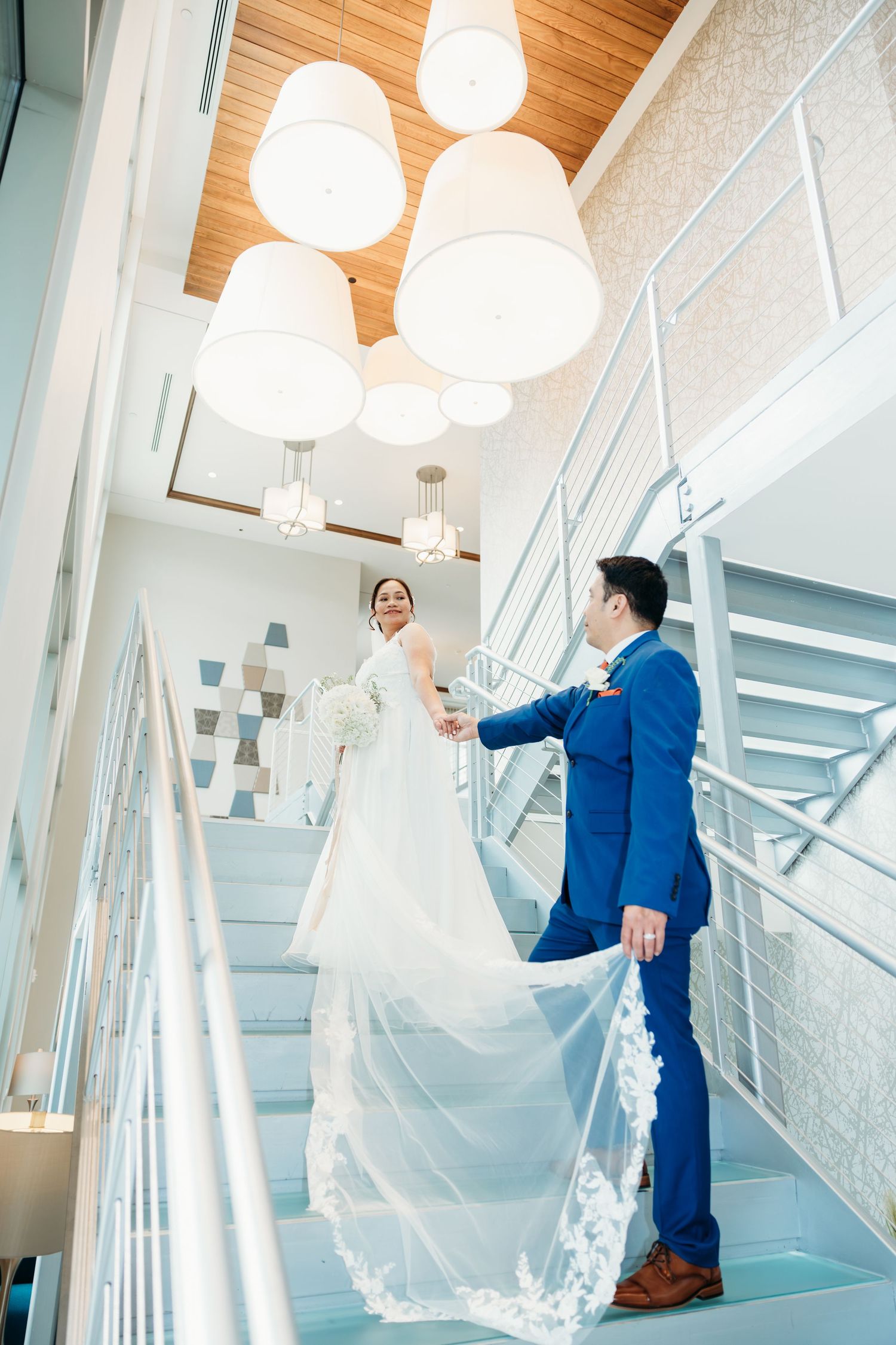Wedding couple shares intimate moment on modern staircase with wooden ceiling and pendant lights.