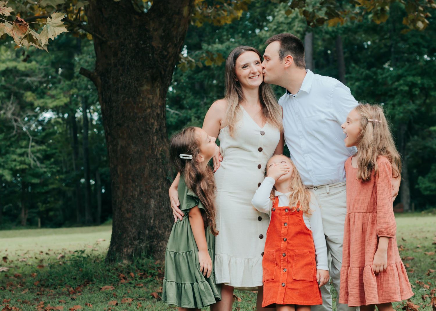 Family poses together in coordinated outfits for outdoor photo session in green park setting.