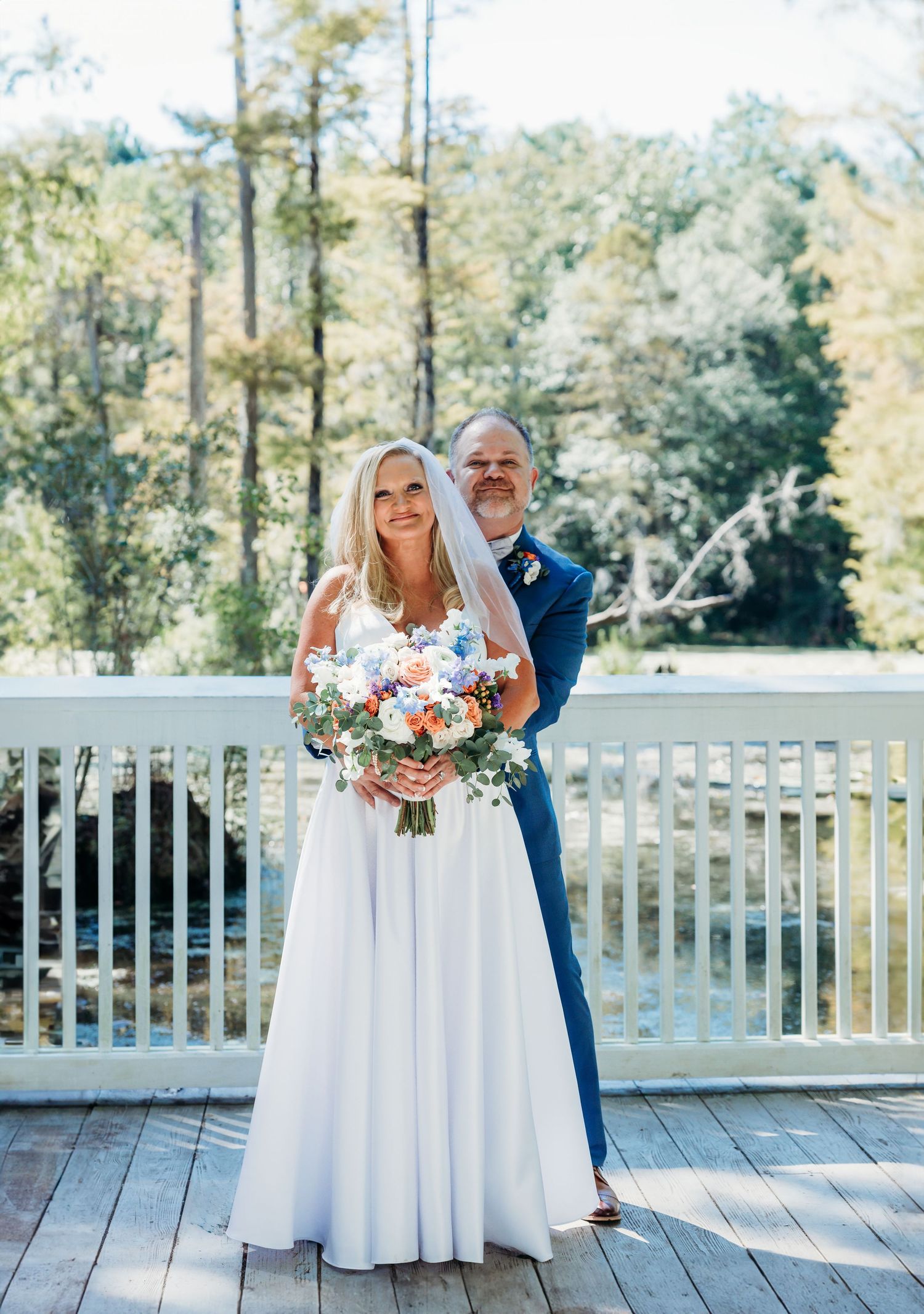 A couple posing on a wooden deck with forest scenery in the background.