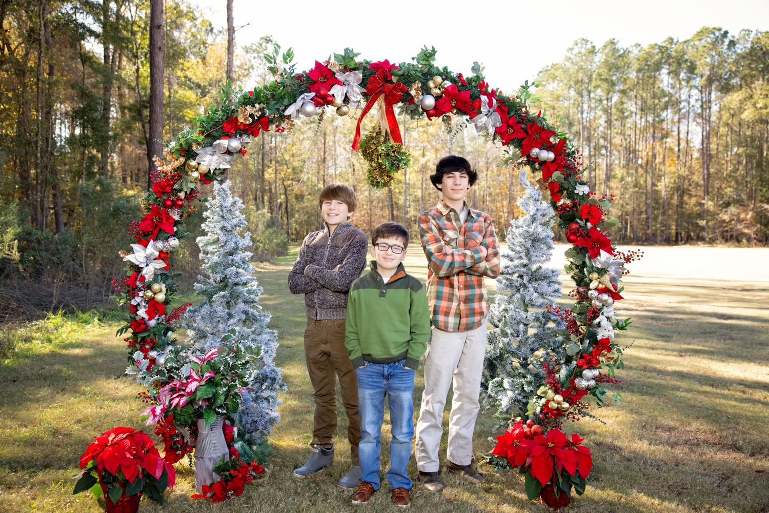 Christmas-themed outdoor family portraits under festive red floral arch.