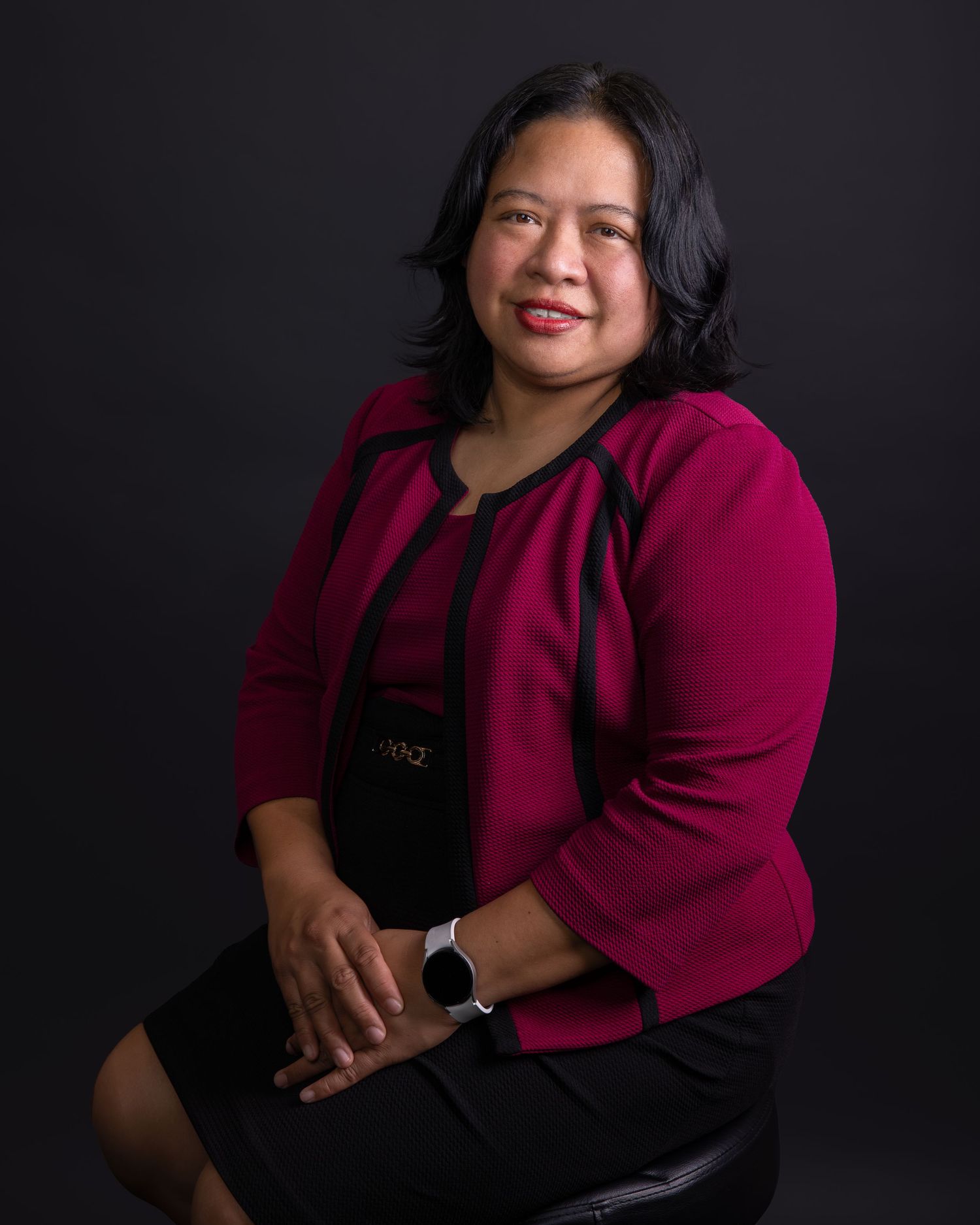 Professional studio portrait against dark background featuring woman in magenta blazer.