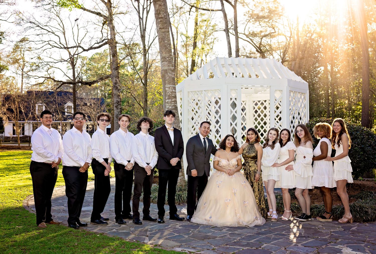 Large wedding party poses in front of white lattice backdrop during outdoor ceremony.