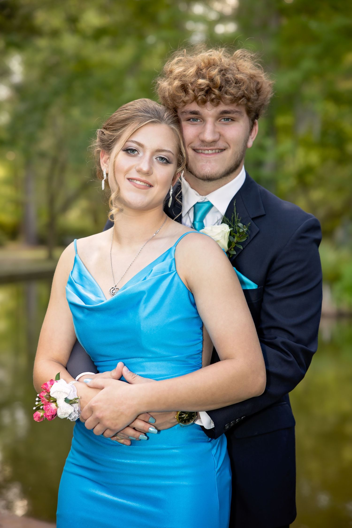 Couple in formal attire poses together outdoors, with person in bright blue dress and person in dark suit.