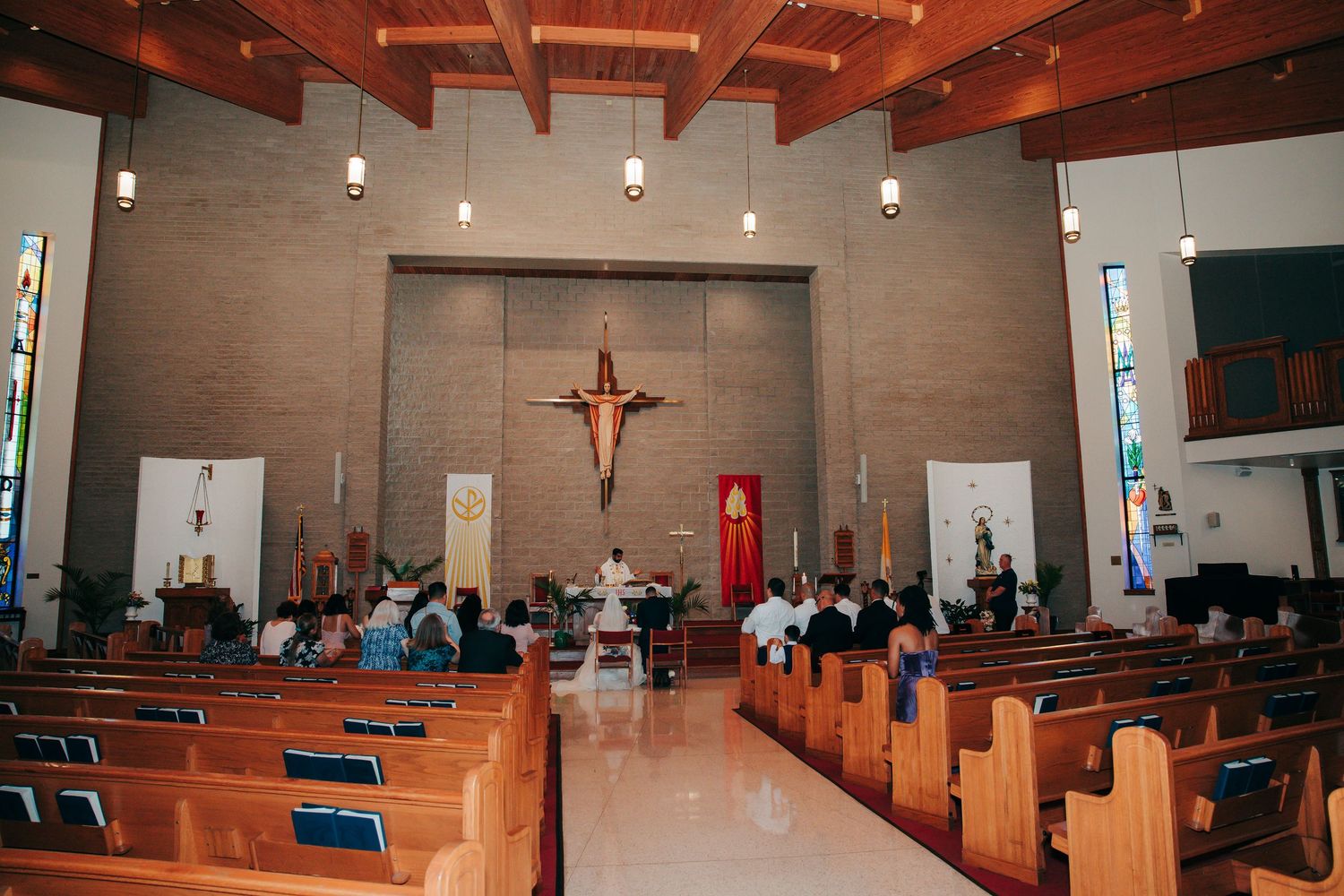 Interior panorama of modern church sanctuary with wooden beams and crucifix on wall.