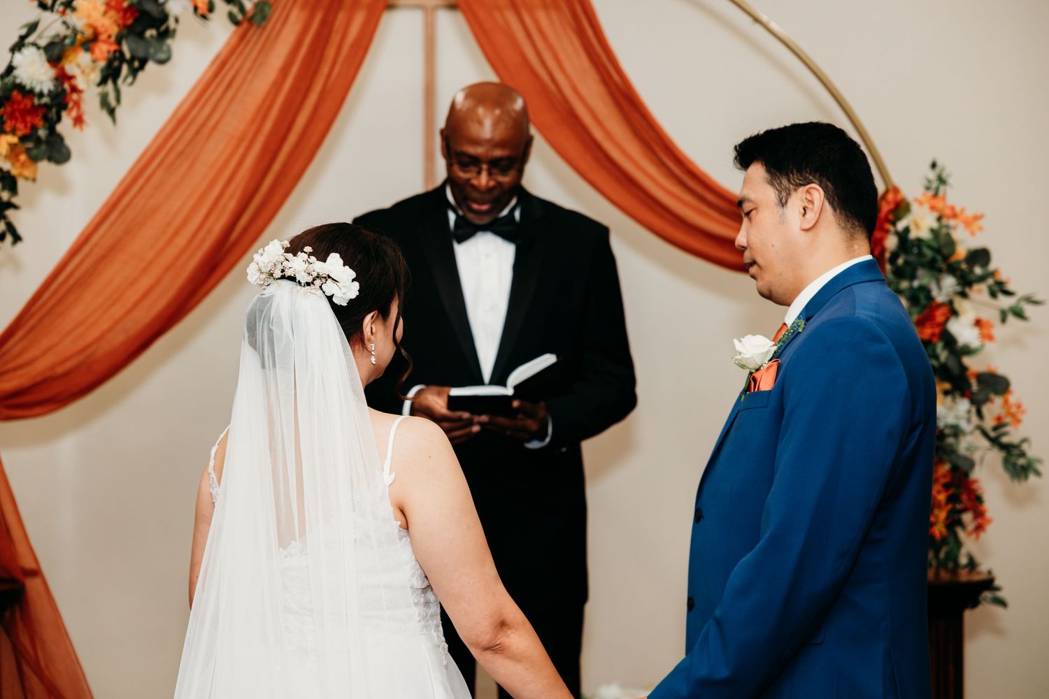 Wedding ceremony moments under an elegant orange draped arch with floral accents.
