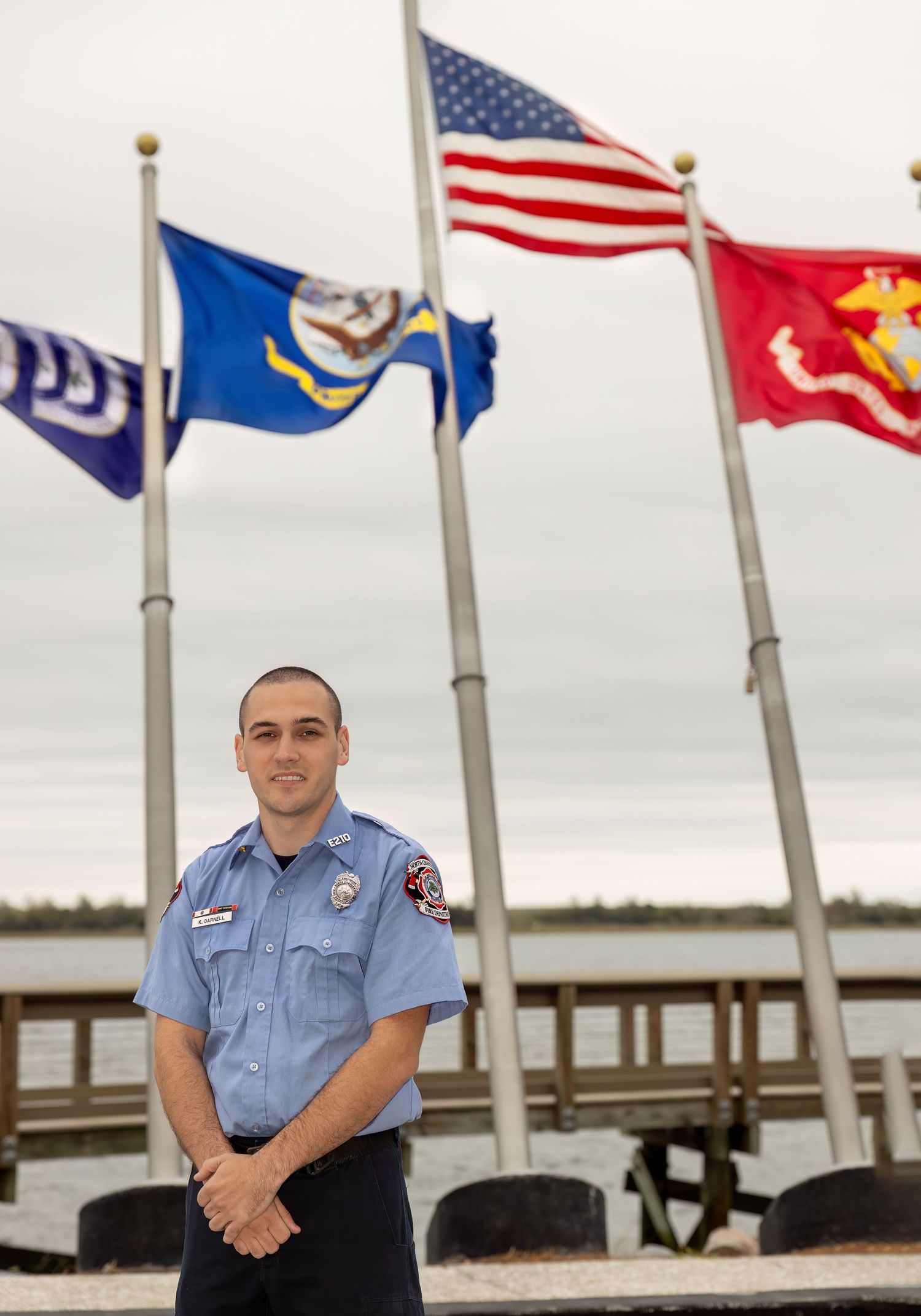 First responder in uniform standing near military flags on waterfront.