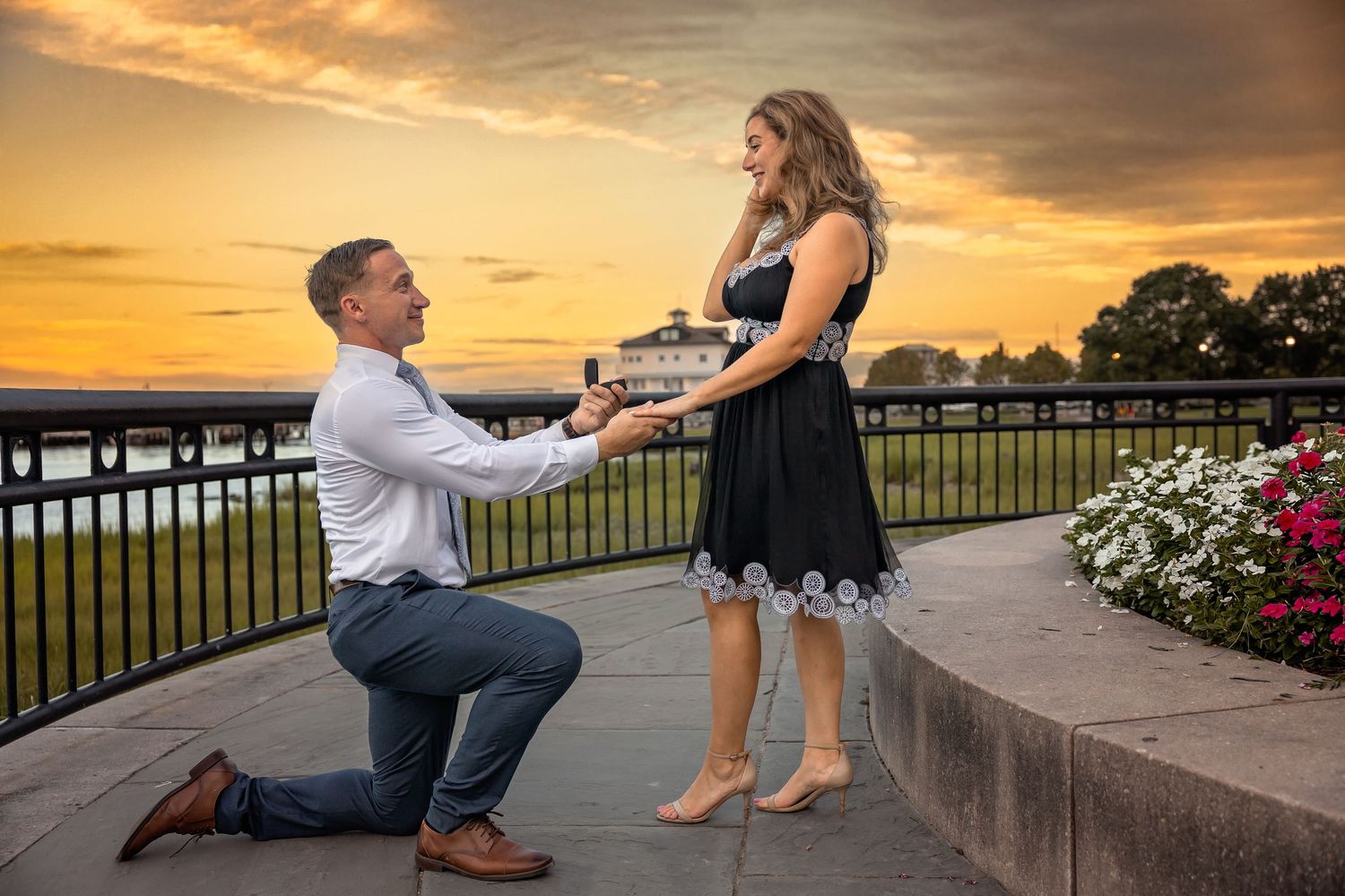 Romantic sunset proposal scene at waterfront with pineapple fountain and pink flowers.