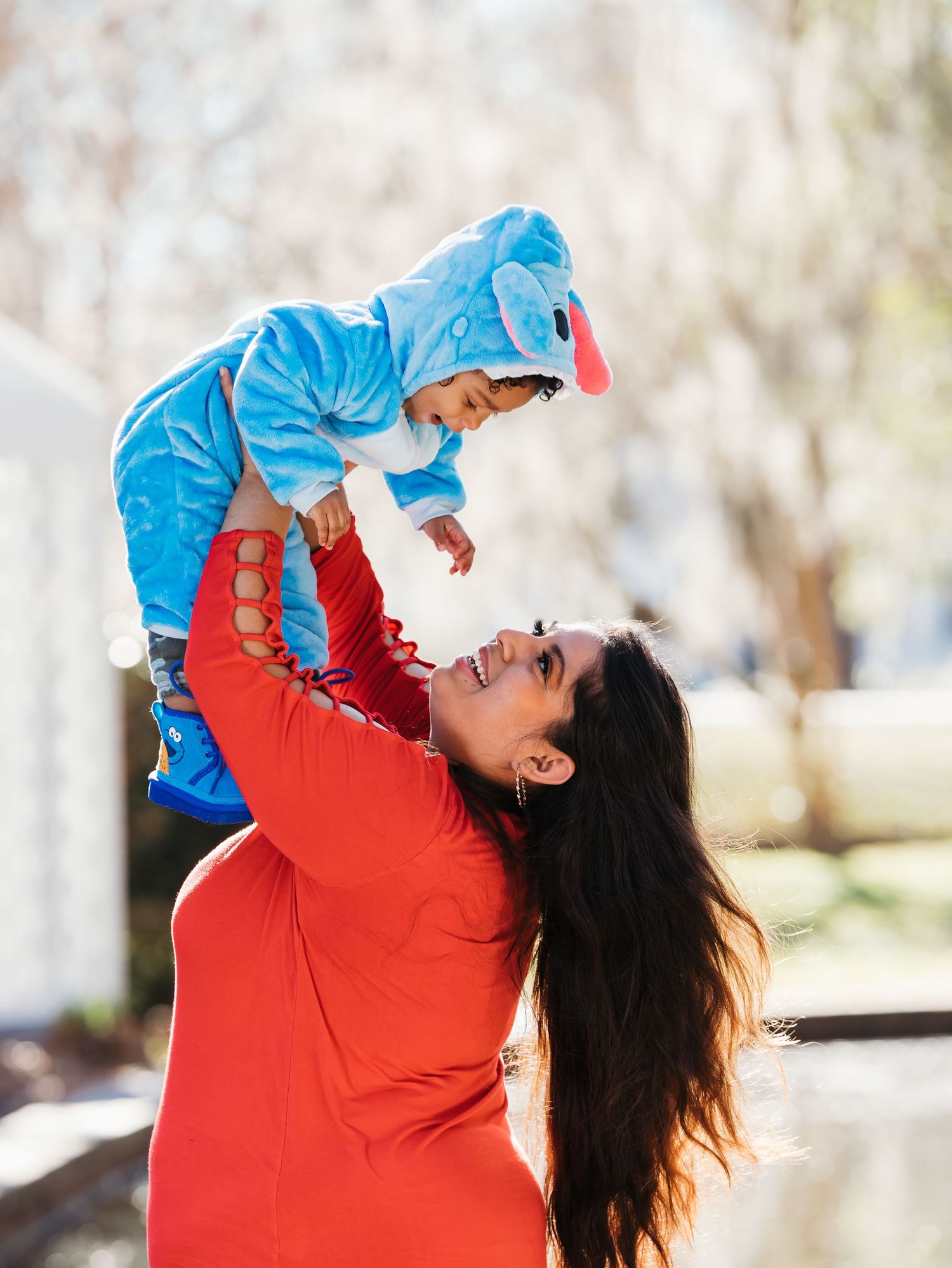 Joyful moment captured as parent lifts child in bright blue outfit against sunny outdoor background.