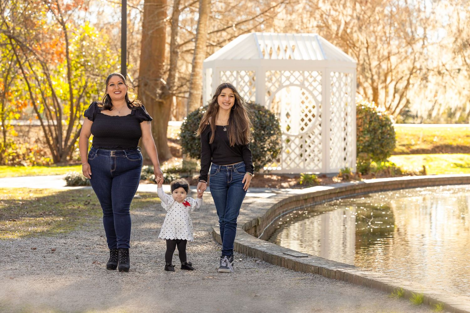 Family walking together on garden path with white lattice gazebo in background.