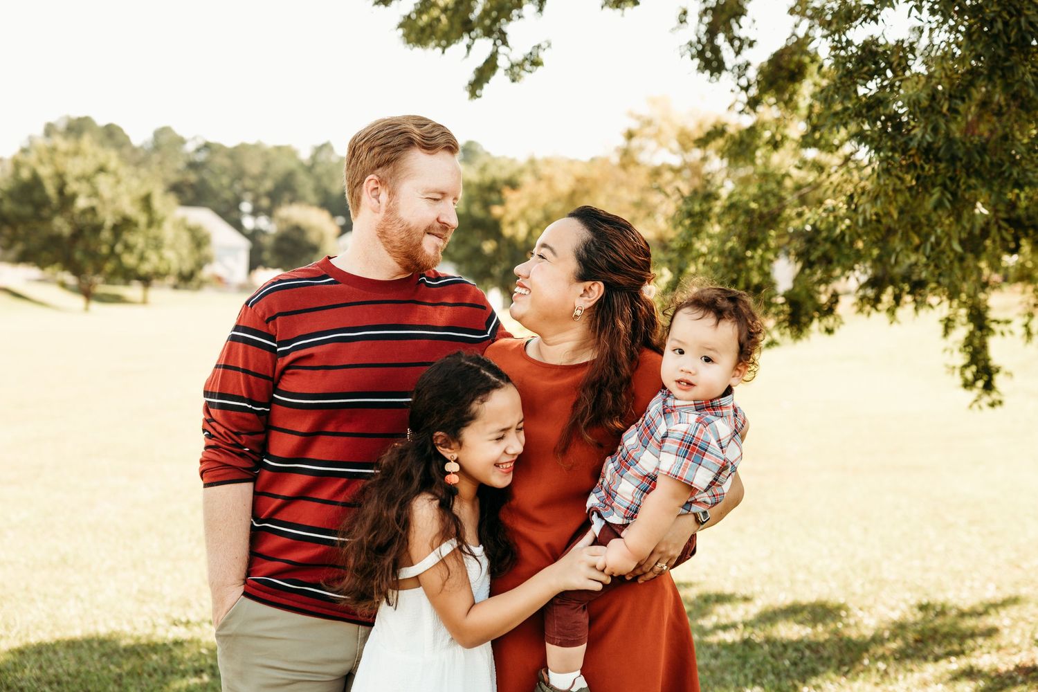 Happy family in red and white outfits plays together on grassy hill during golden hour.