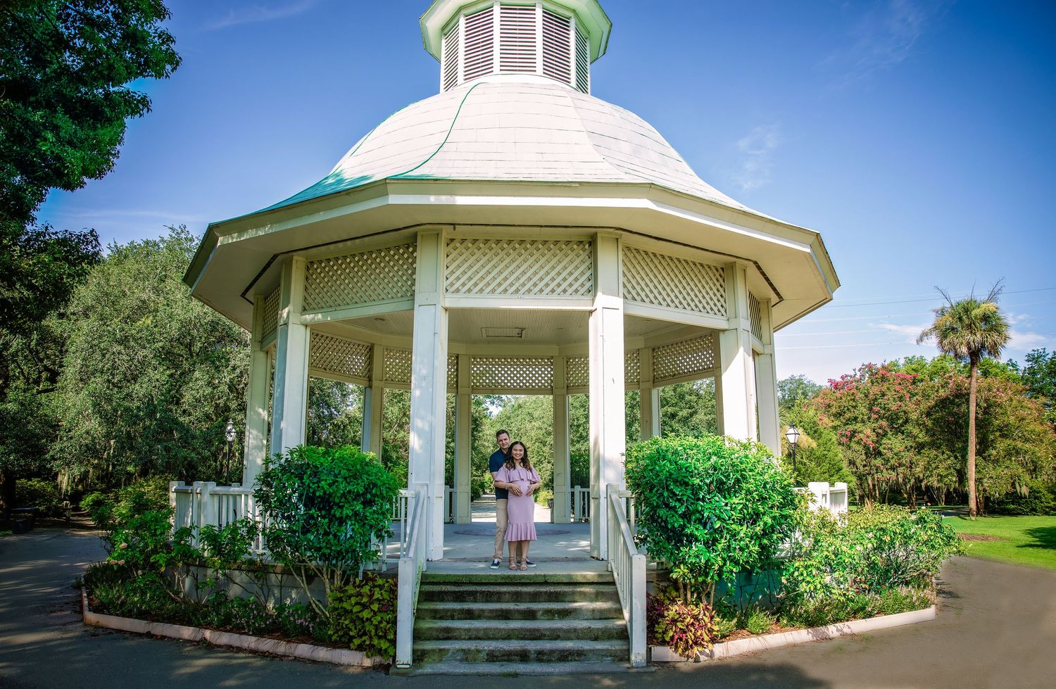 Panoramic view of a white gazebo structure with green dome in a lush garden setting.