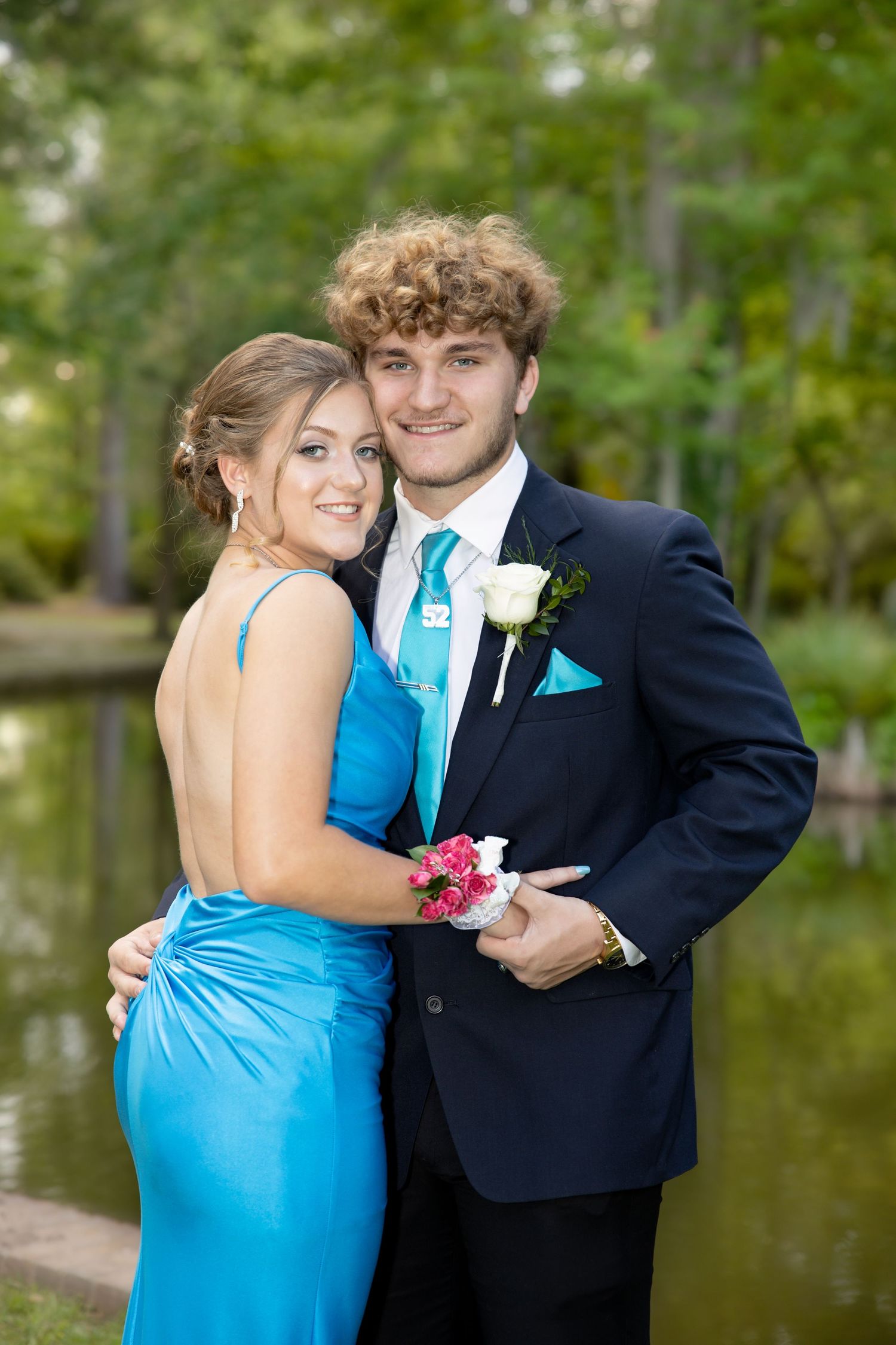 Couple embraces during formal photo session by a lake with trees in background.
