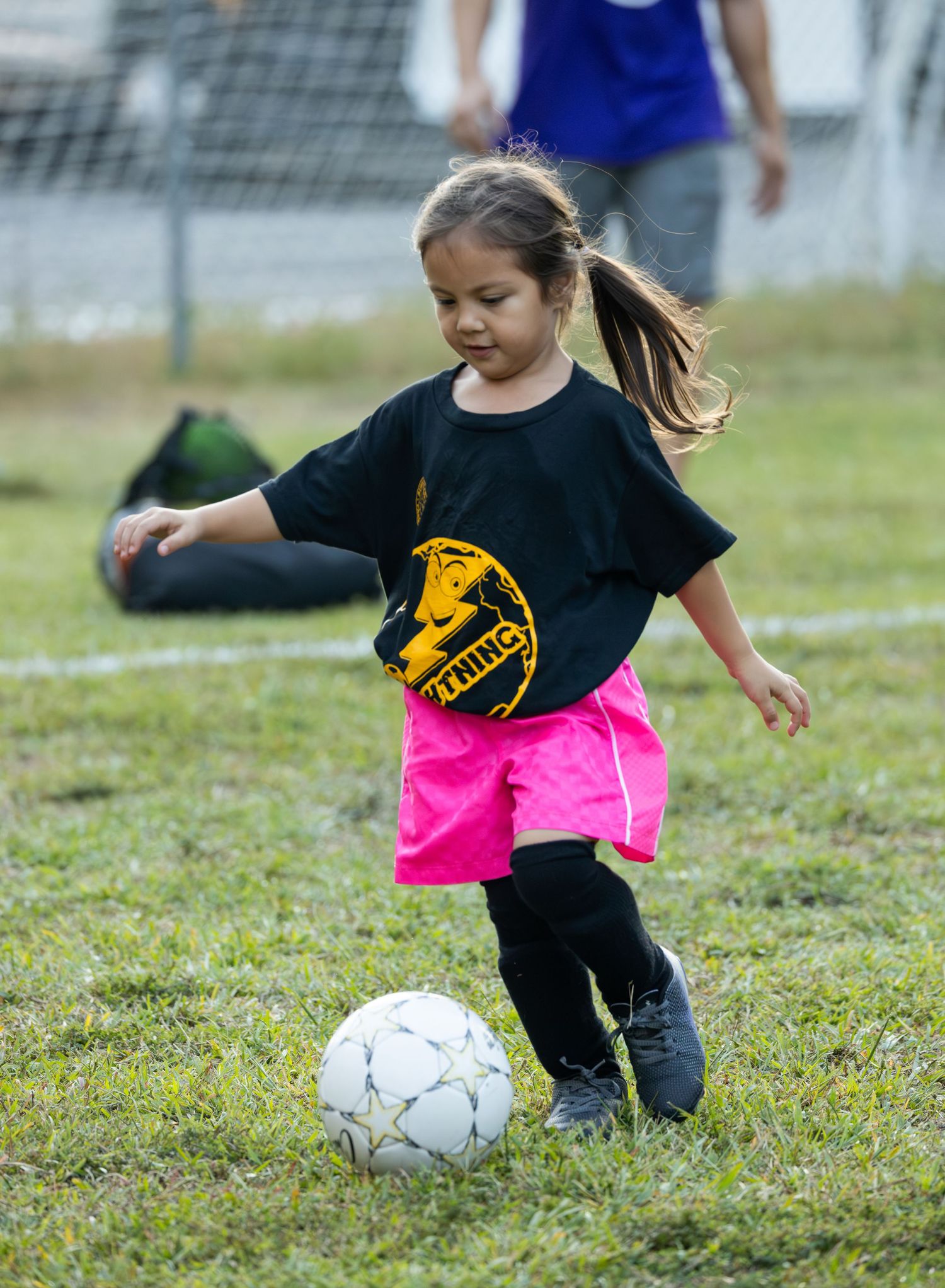 Children practicing soccer drills with black and pink uniforms on a grassy field.