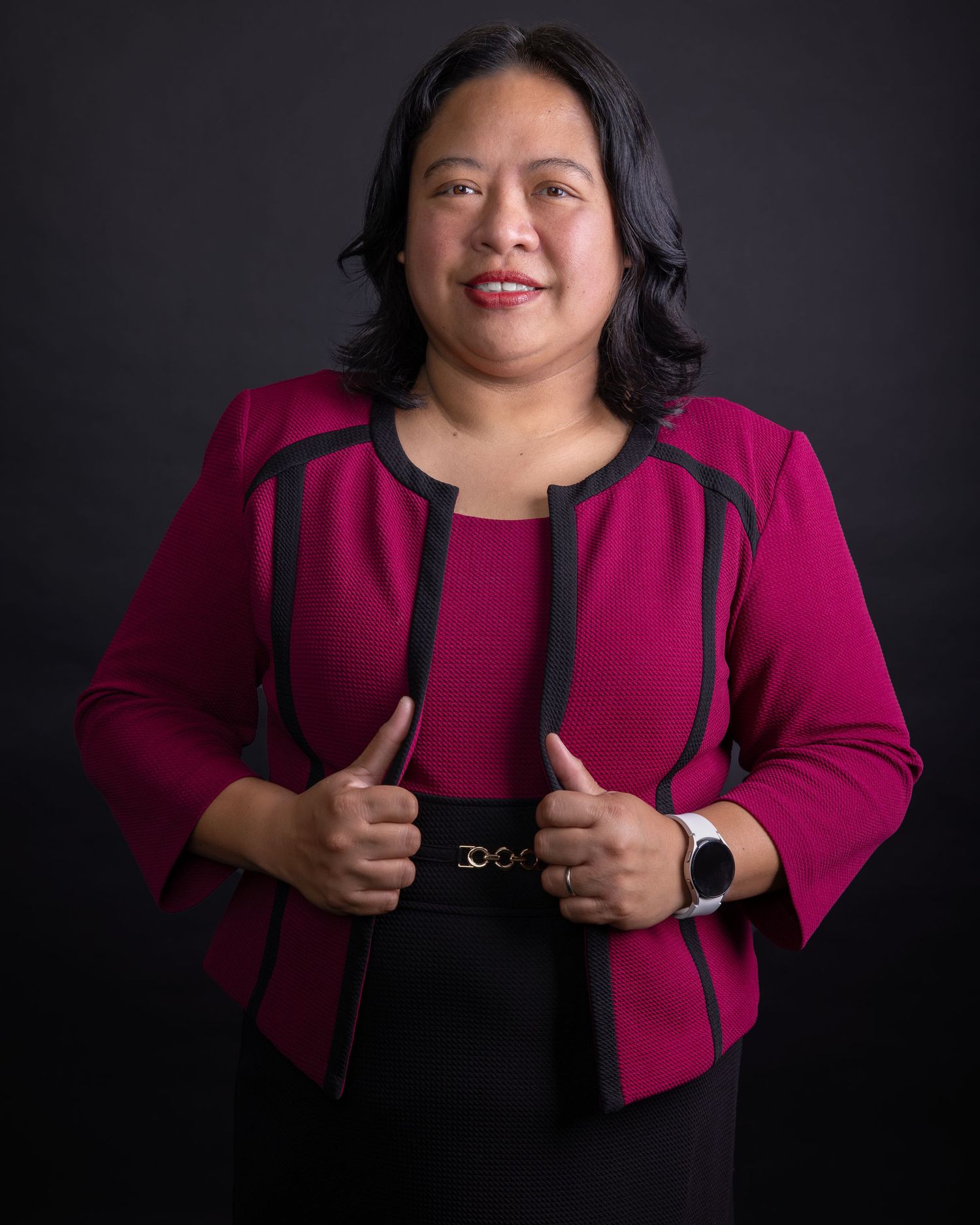 Woman in bright pink blazer poses confidently against black backdrop.
