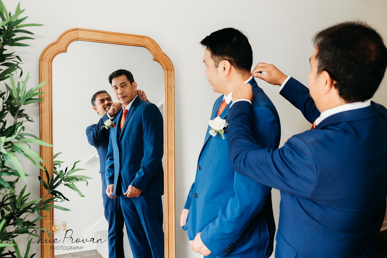 Groomsmen in navy suits helping with wedding preparations in front of ornate mirror.