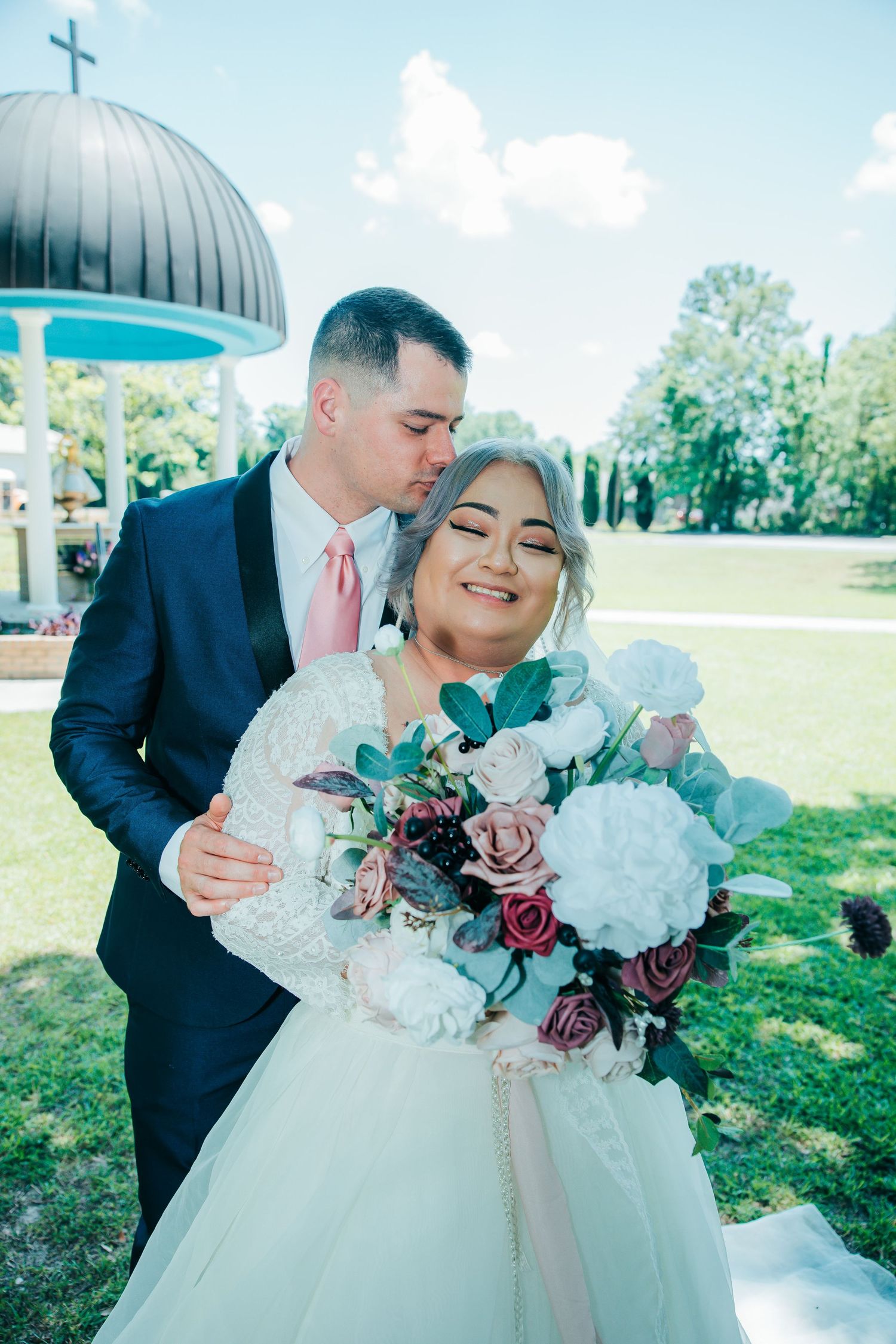 Bride holding a beautiful bouquet of burgundy and white flowers on a sunny outdoor wedding day.